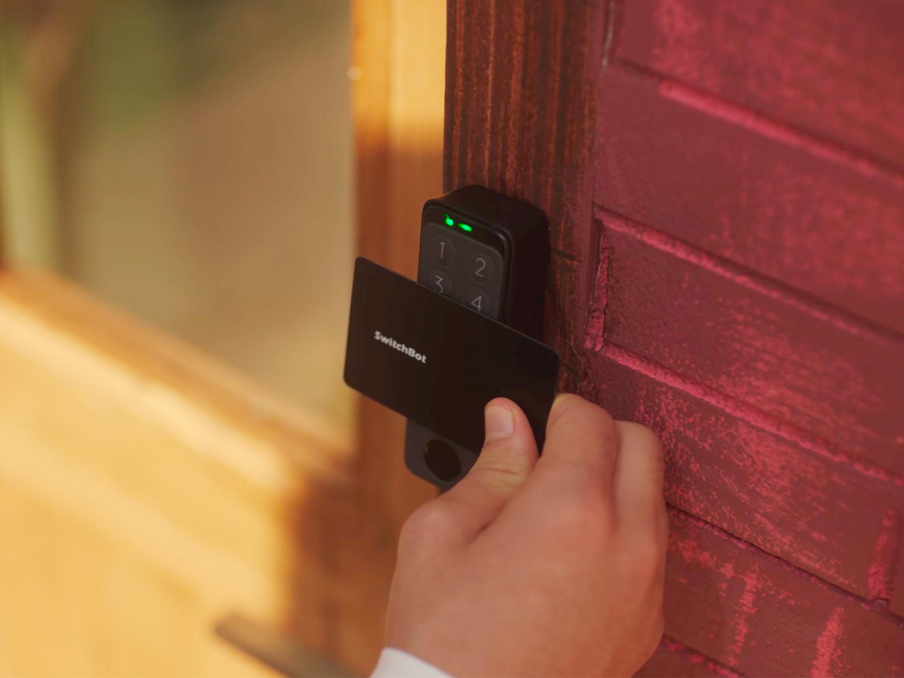 Eine Hand, die eine SwitchBot-Karte verwendet, um ein SwitchBot-Tastenfeld an einer Holztür zu entsperren.