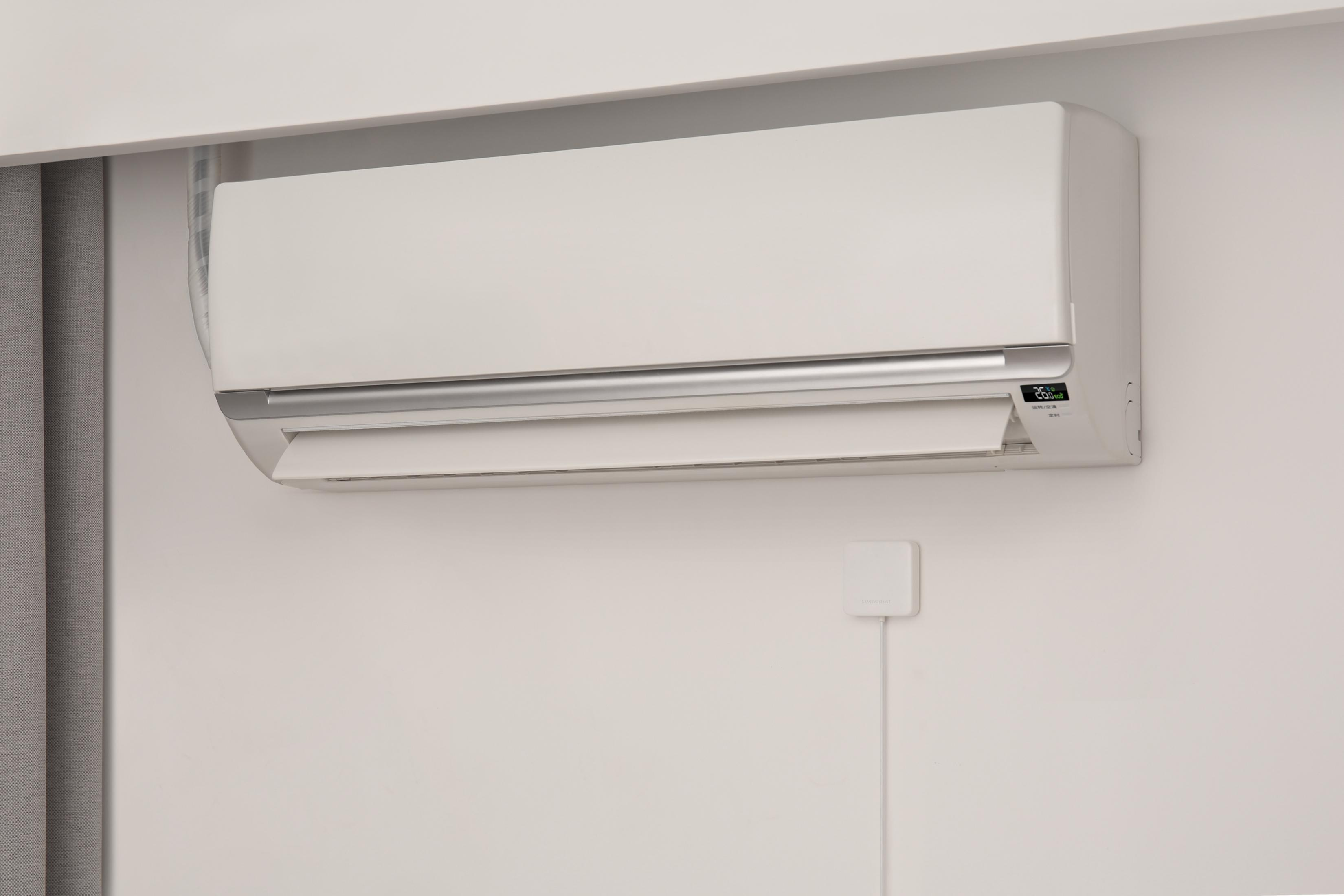Eine weiße Klimaanlage an einer weißen Wand mit einem SwitchBot-Hub darunter.