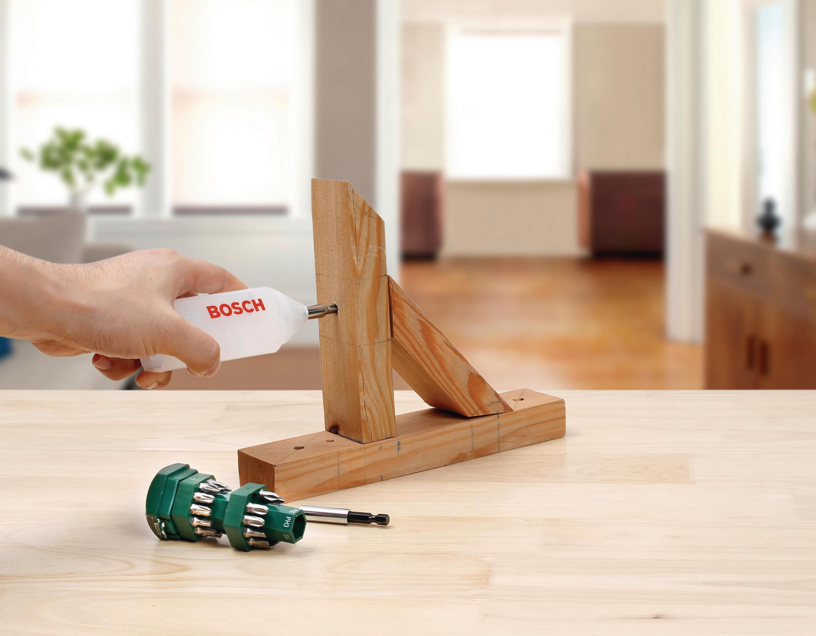 Un tournevis Bosch est utilisé pour visser deux morceaux de bois ensemble sur une table en bois.