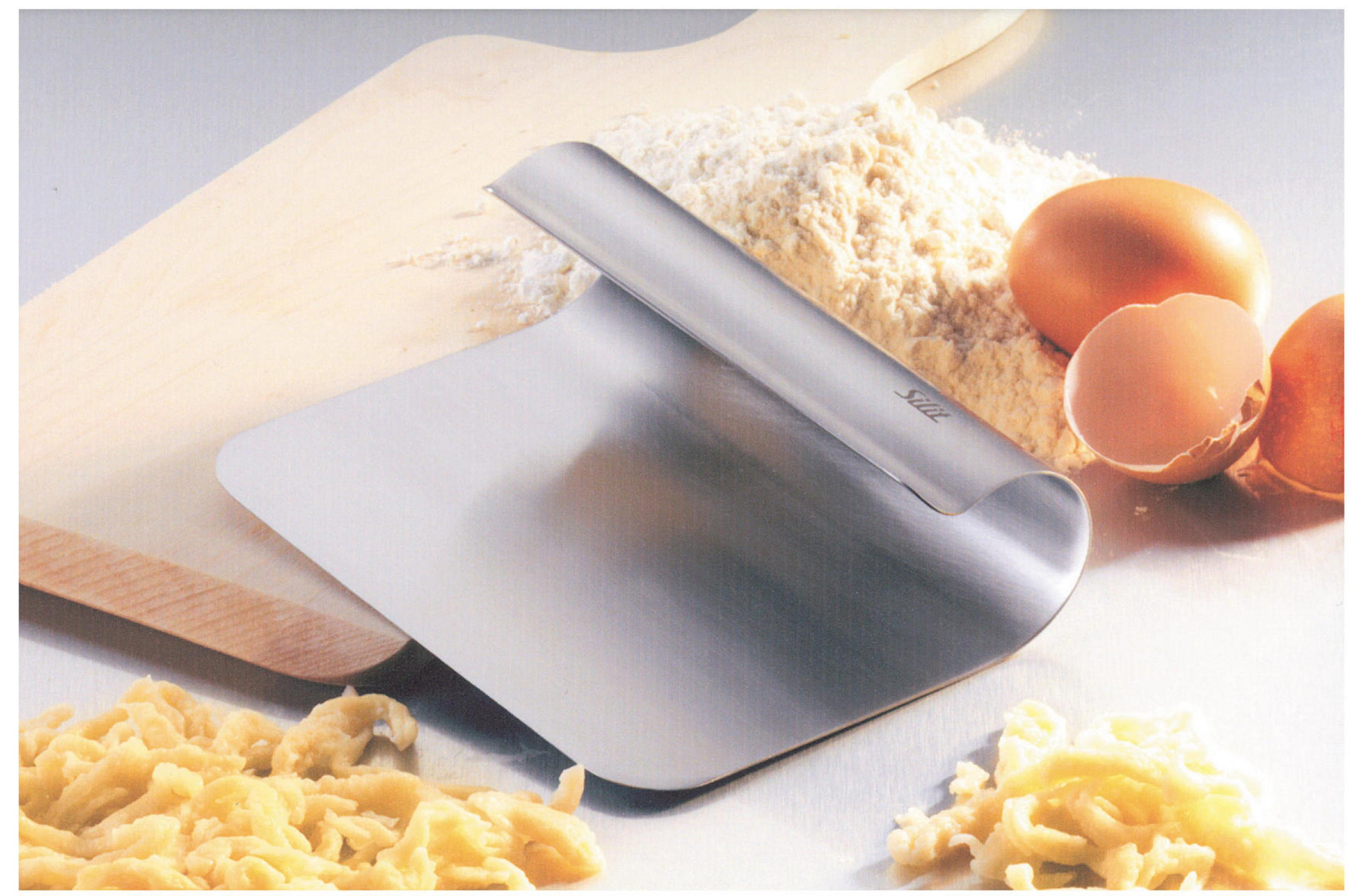 Ein Teigschaber auf einem Holzbrett mit Mehl, Eiern und Käse.