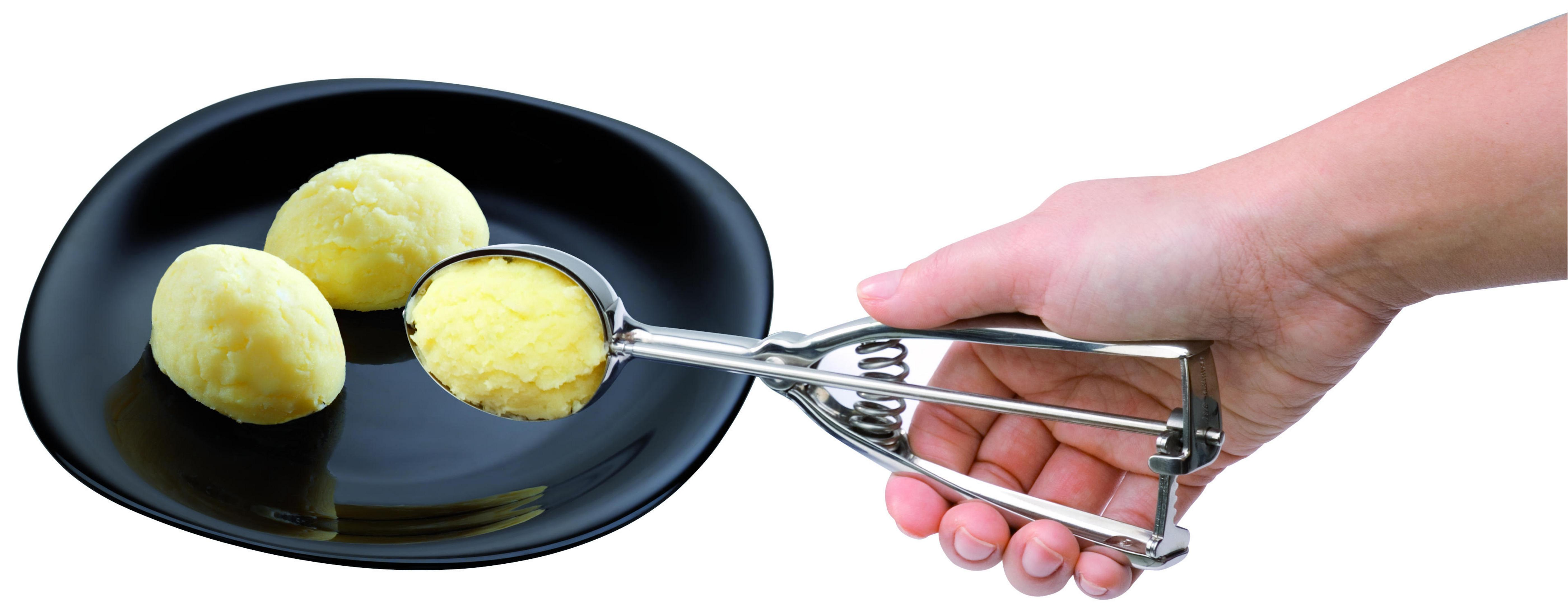 Eine Hand schöpft gelbe Kartoffelpüree mit einem Eisportionierer auf einen schwarzen Teller. Zwei weitere Kugeln sind vorhanden.