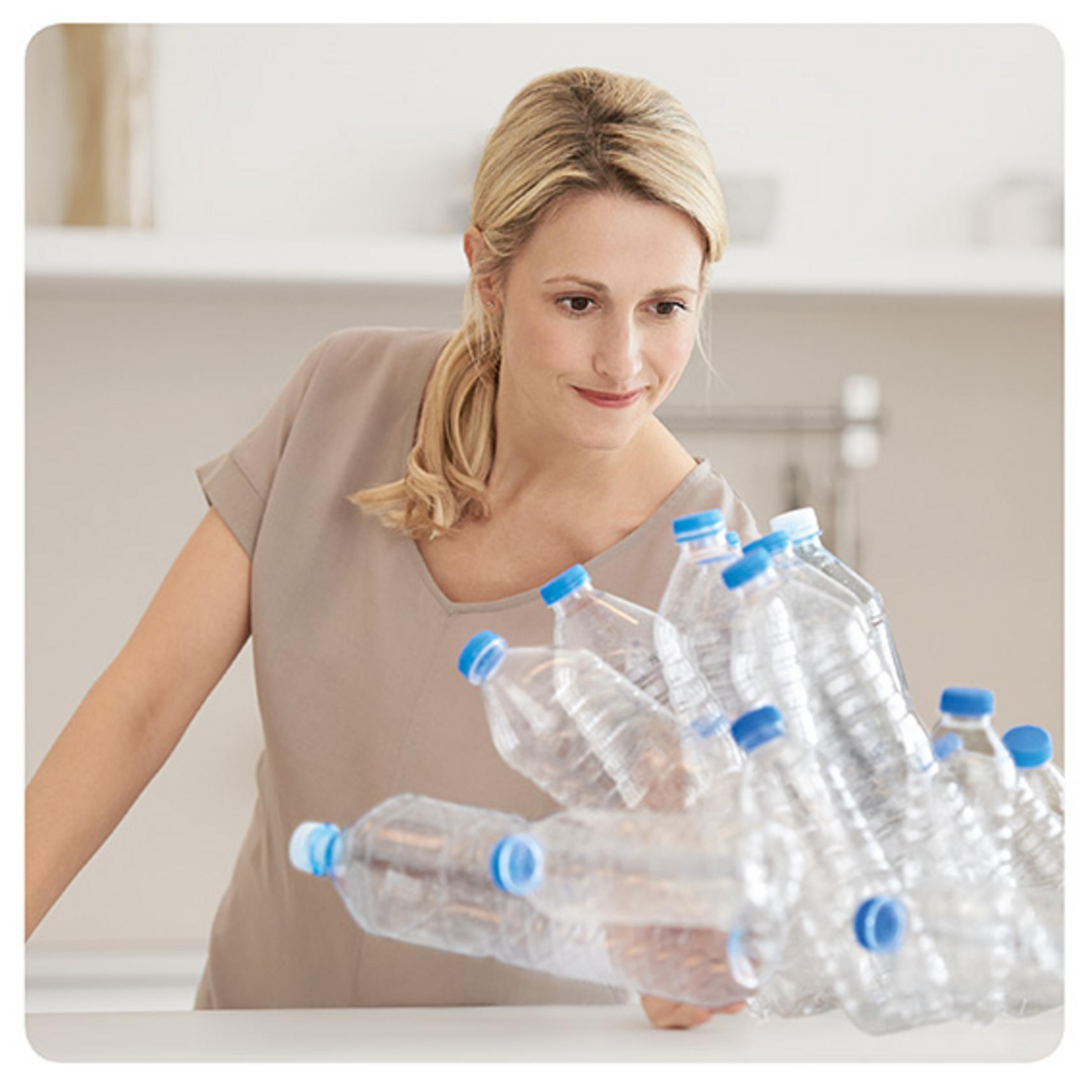 Woman with blonde hair looking at a pile of clear plastic water bottles with blue caps.