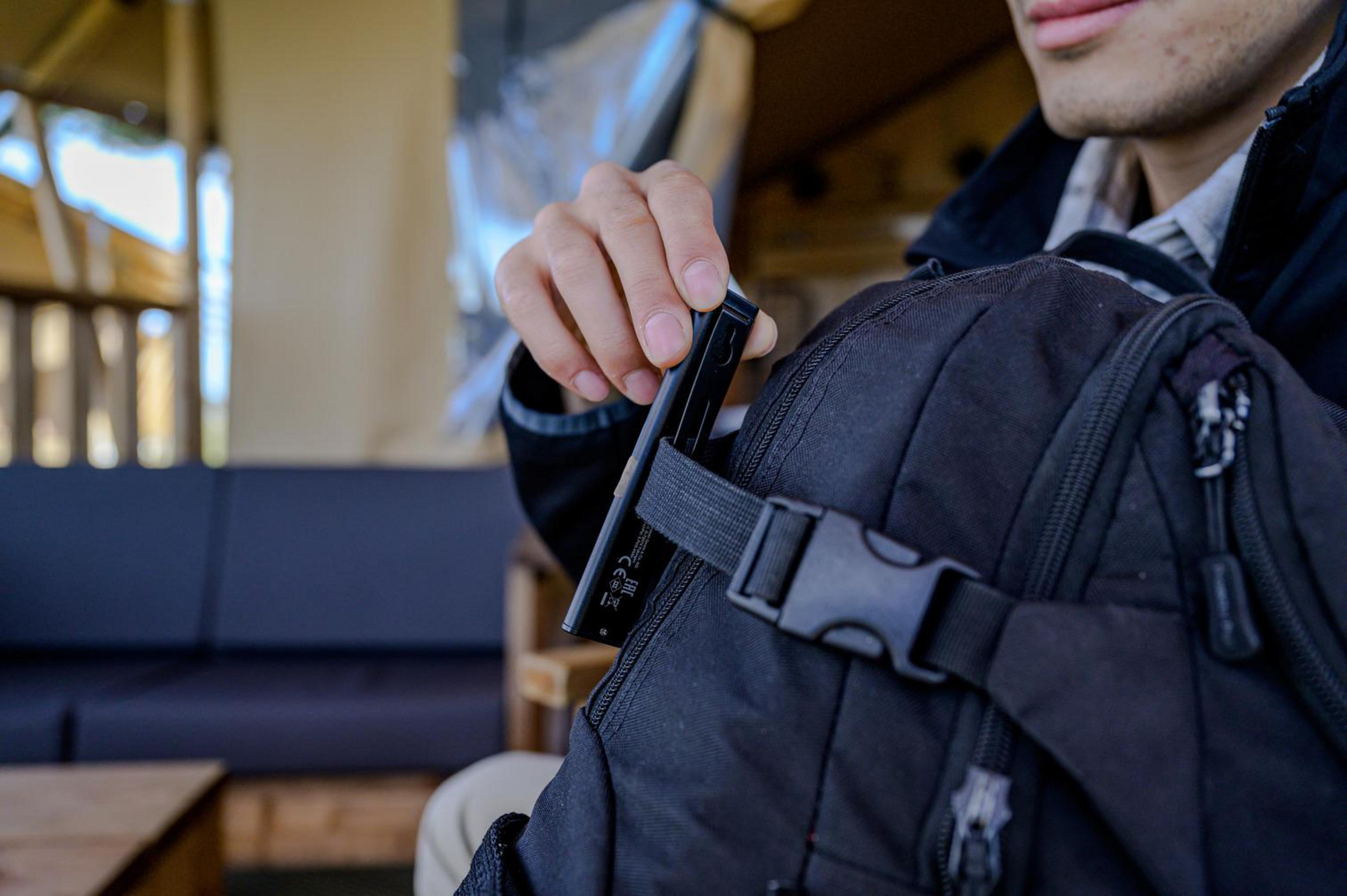 Eine Person steckt eine schwarze Arbeitsleuchte in einen schwarzen Rucksack im Freien.