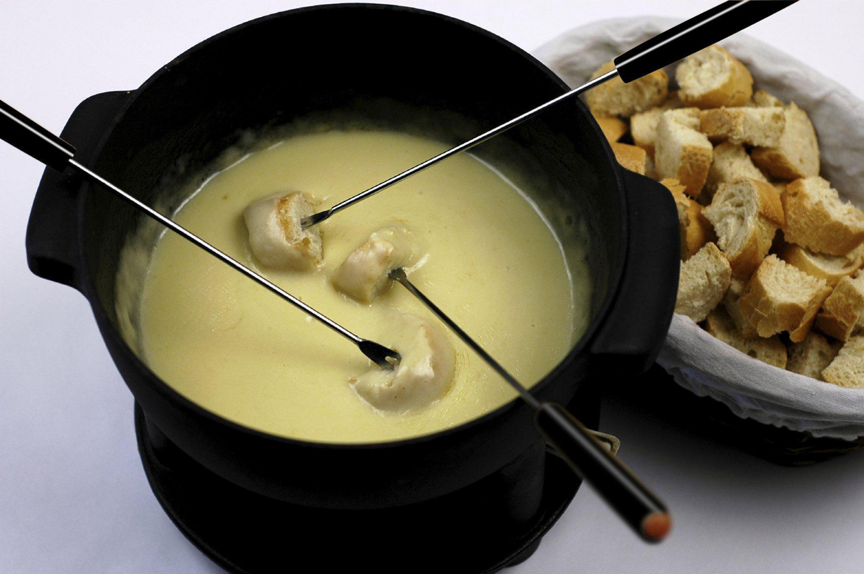 Fonduetopf mit Käse und Brot. Drei Gabeln mit Brot im Käse. Weißer Hintergrund.