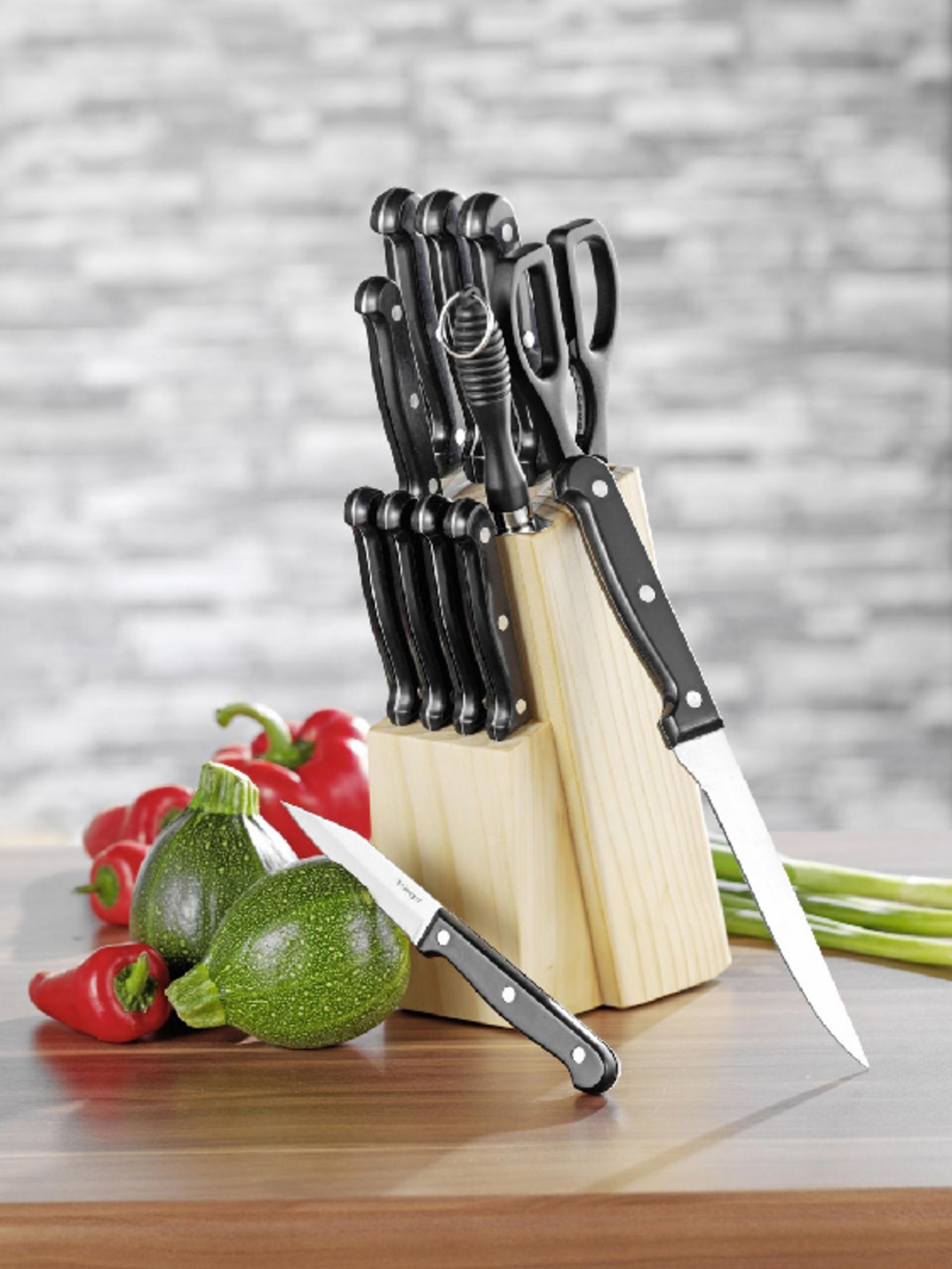 Ein Messerblock mit Messern mit schwarzen Griffen, Zucchini, Paprika und Frühlingszwiebeln auf einer Holzoberfläche.