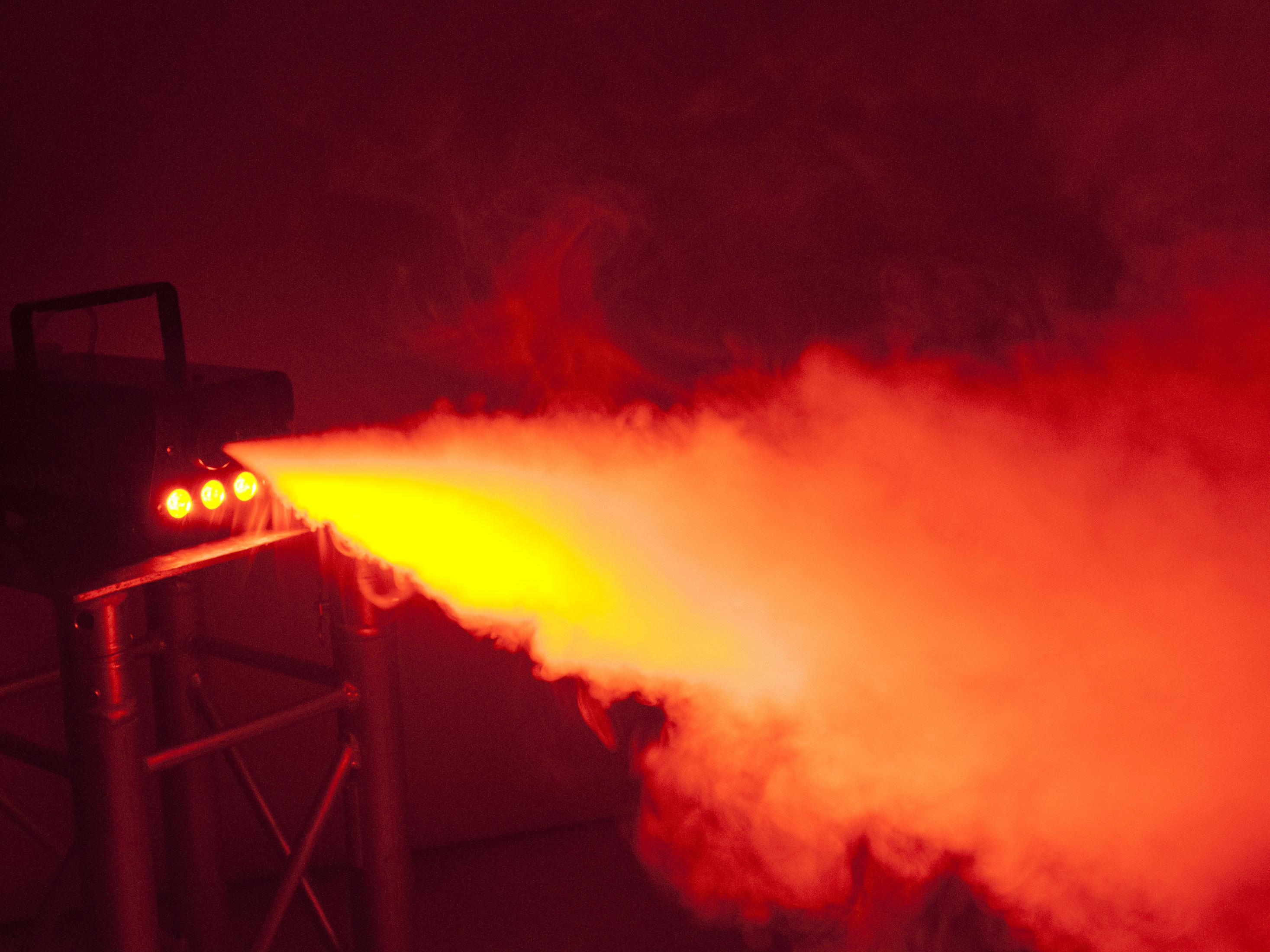Eurolite N-11 Nebelmaschine, die gelben Rauch in einem rot beleuchteten Raum erzeugt. Die Maschine steht auf einem Metallständer.