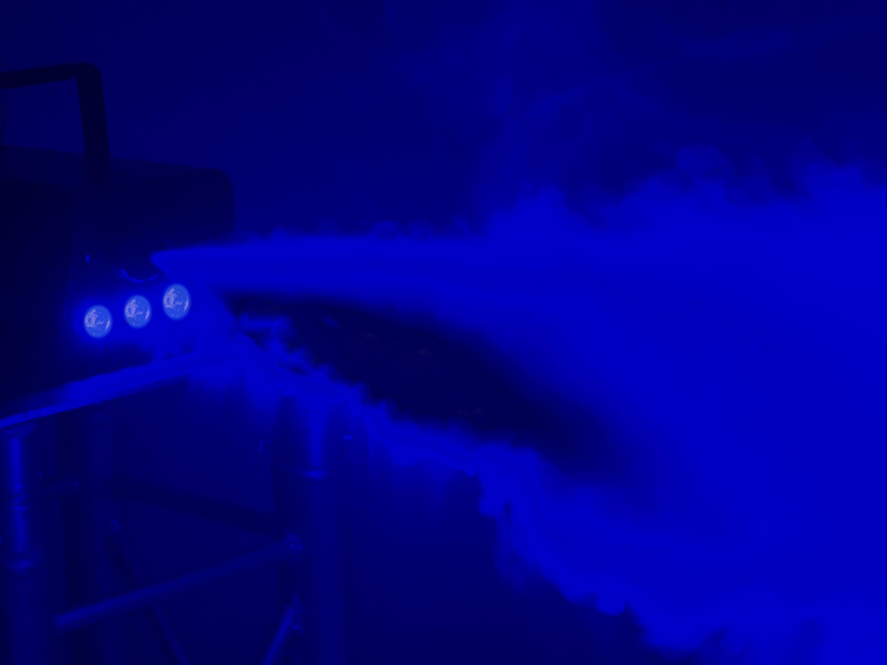Nebelmaschine, die blauen Rauch mit blauen Lichtern auf weißem Hintergrund ausstößt.