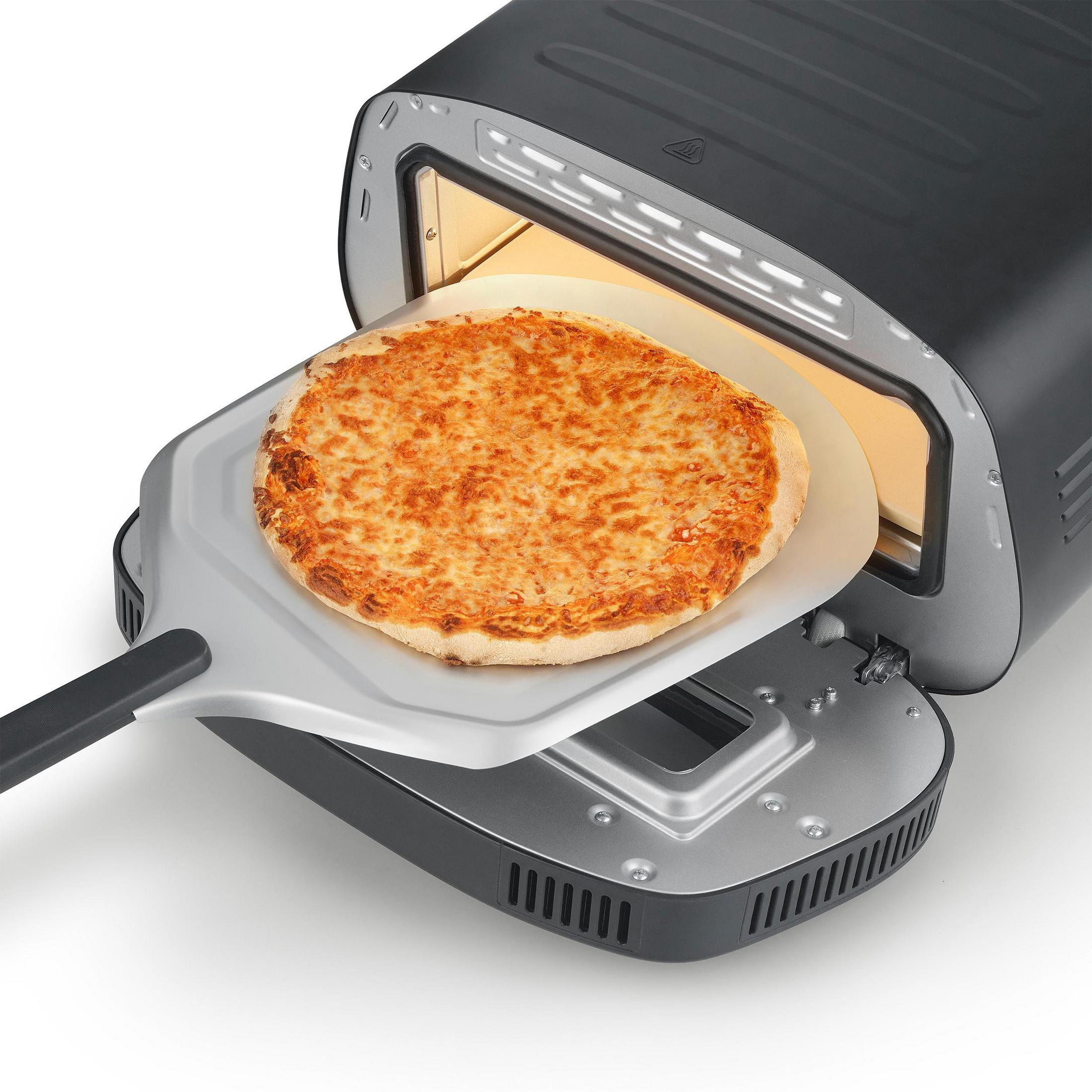 Eine Pizza auf einem Metallschieber wird in einen schwarzen Pizzaofen geschoben.