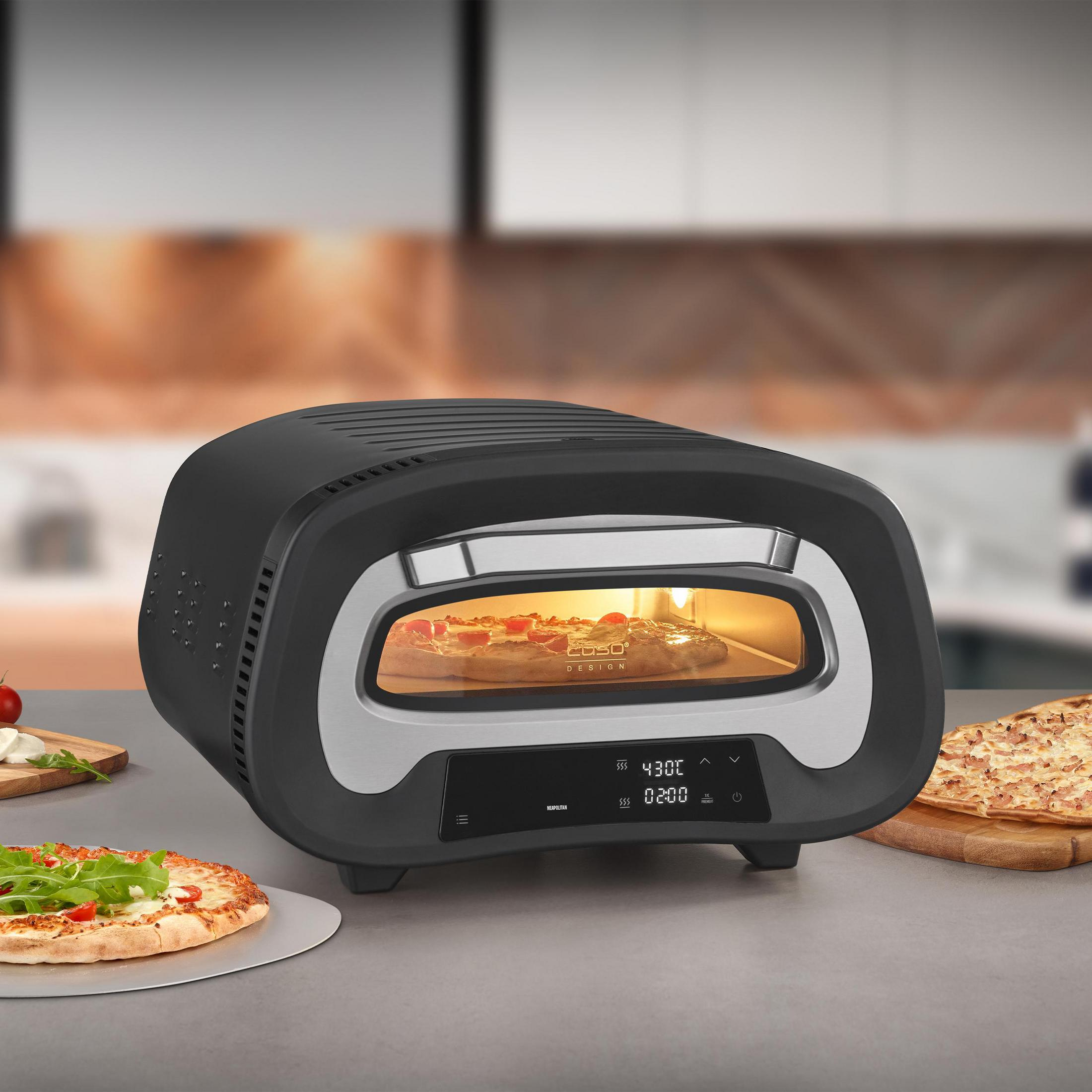 Ein schwarzer und silberner Pizzaofen mit Pizzen drumherum in einer Küchenumgebung.