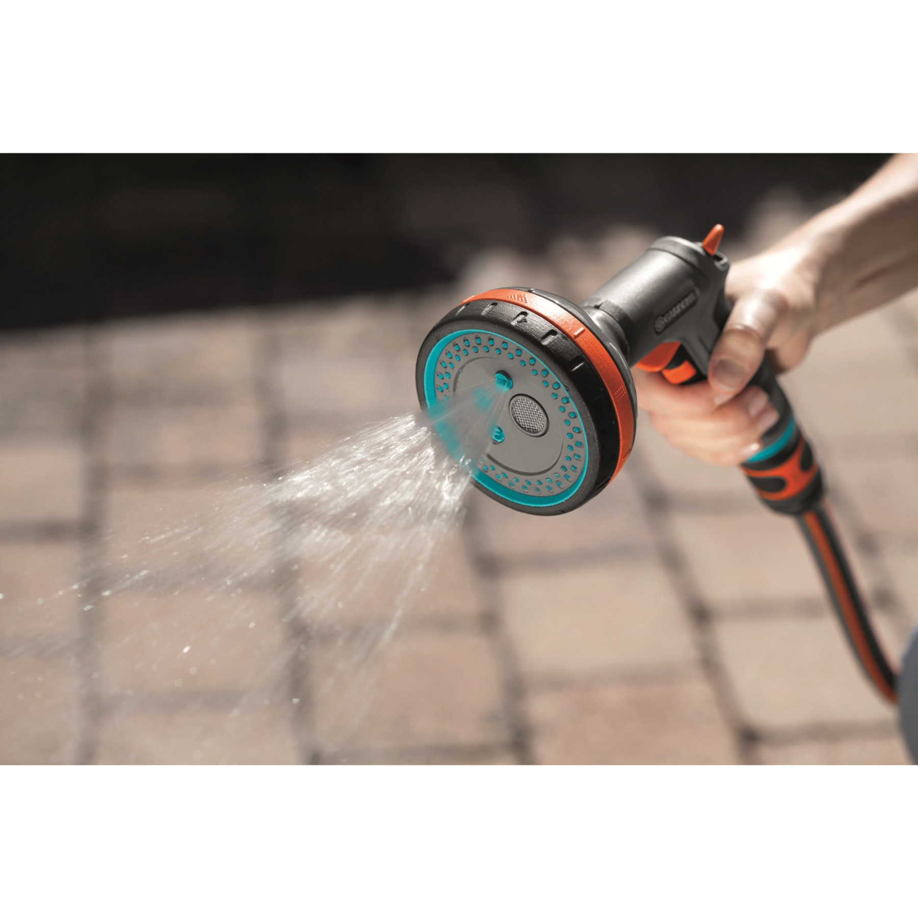 Una mano tiene in mano un nebulizzatore Gardena che emette acqua su uno sfondo di mattoni.
