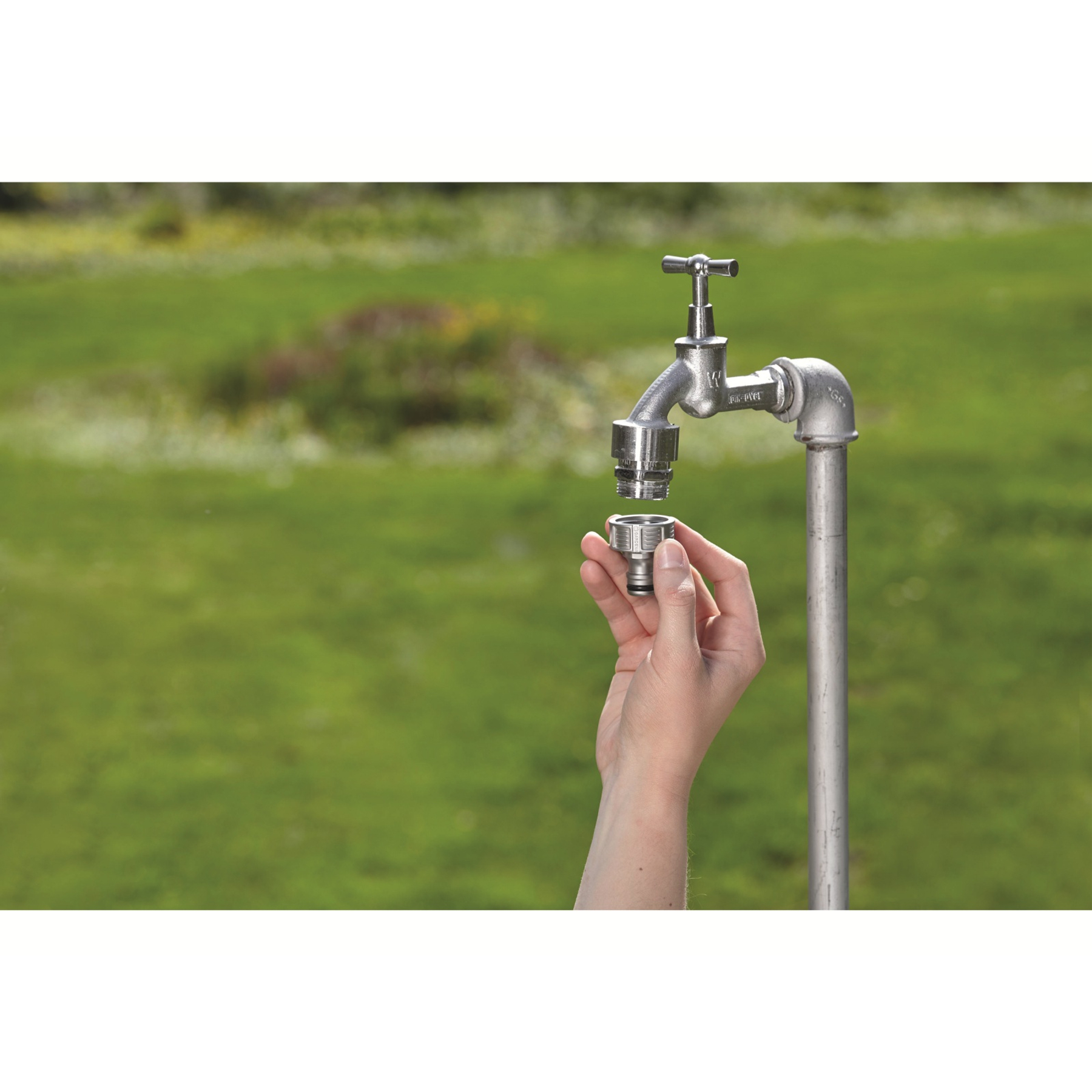 Una mano che installa un connettore per tubo flessibile Gardena a un rubinetto in un ambiente esterno verde.