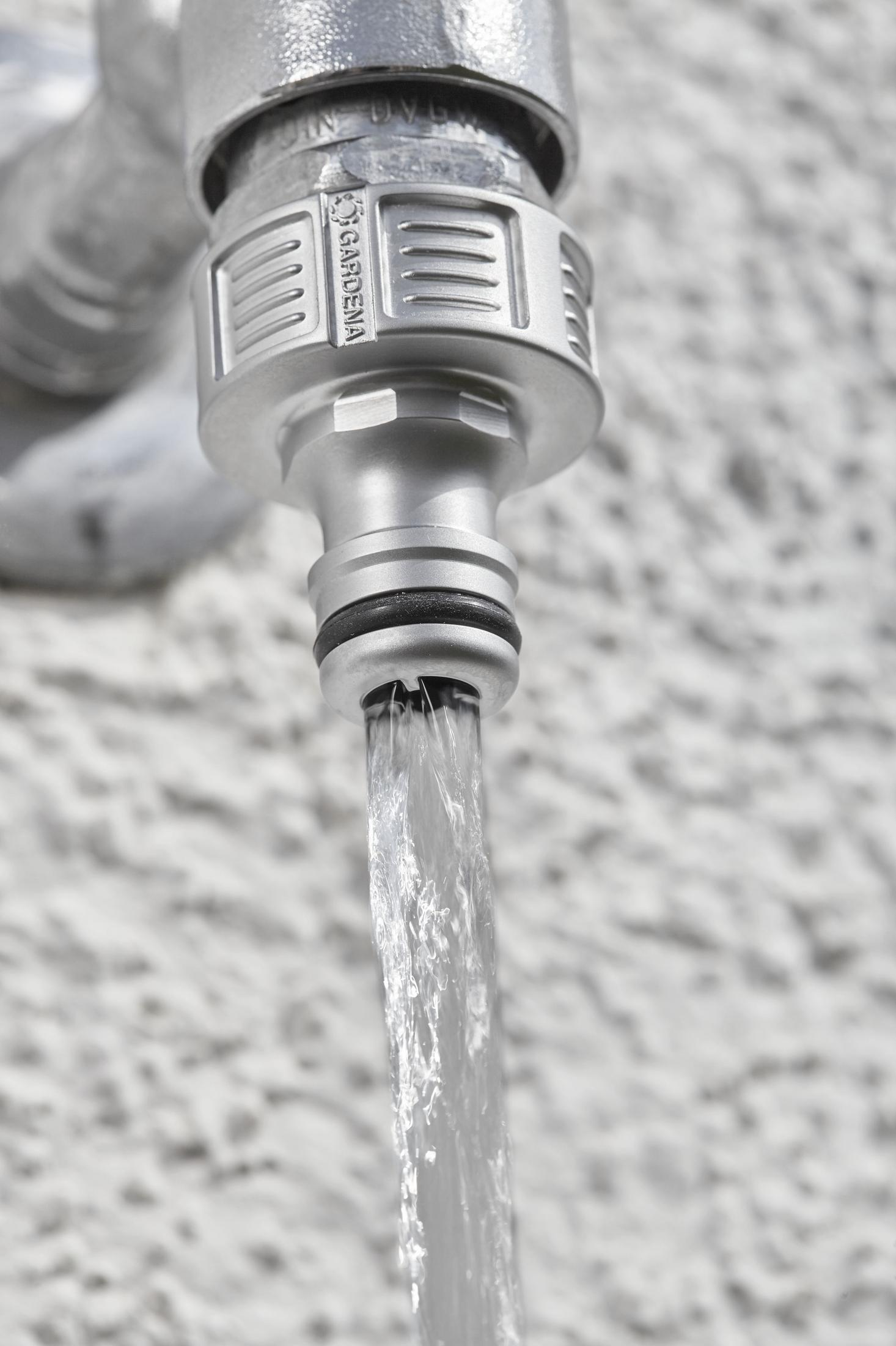 Un rubinetto argentato con acqua che scorre contro un muro bianco ruvido.