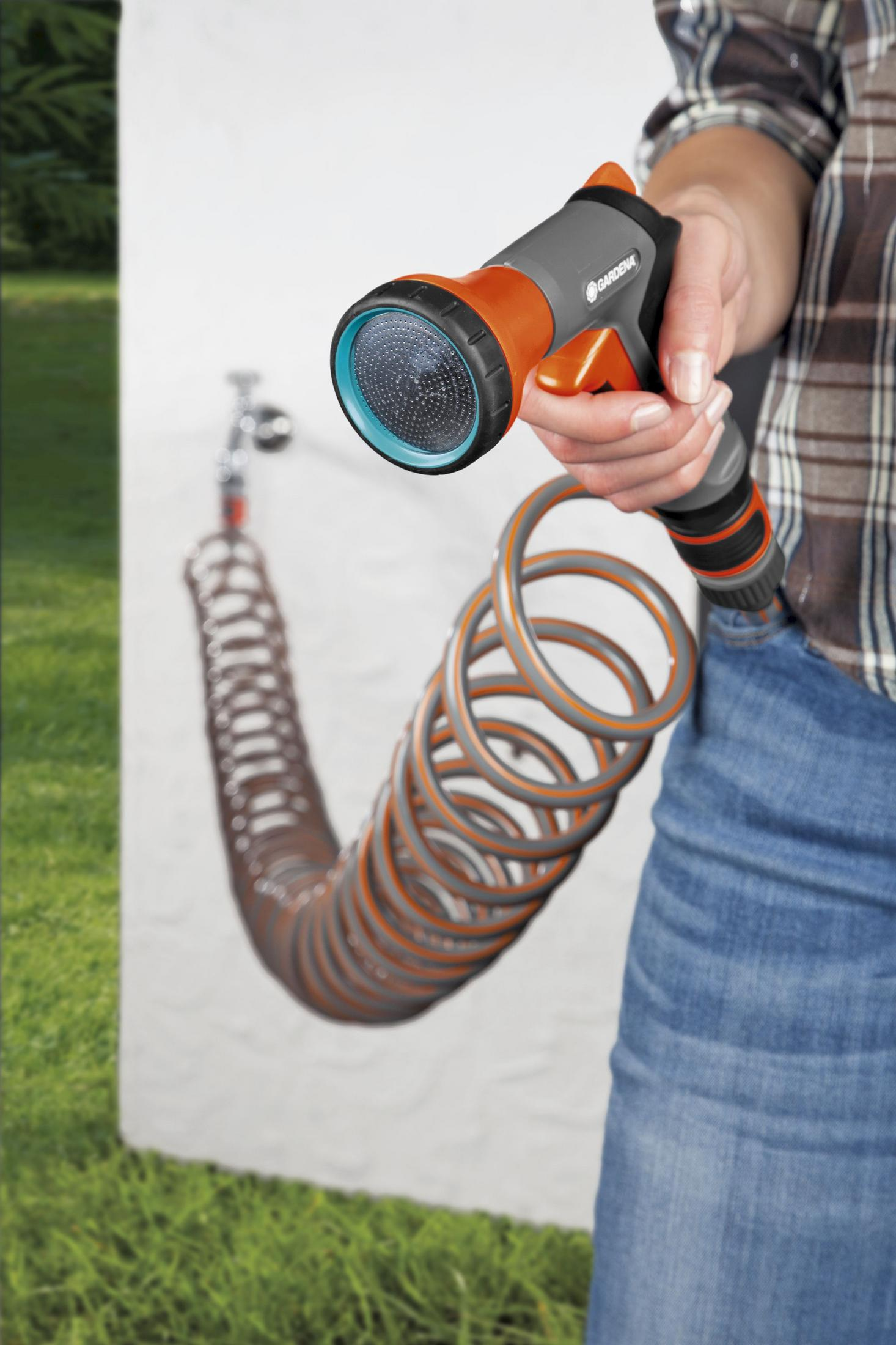 Eine Person hält eine GARDENA Düse, die an einen orange-grauen Schlauch angeschlossen ist, an einer Wand.