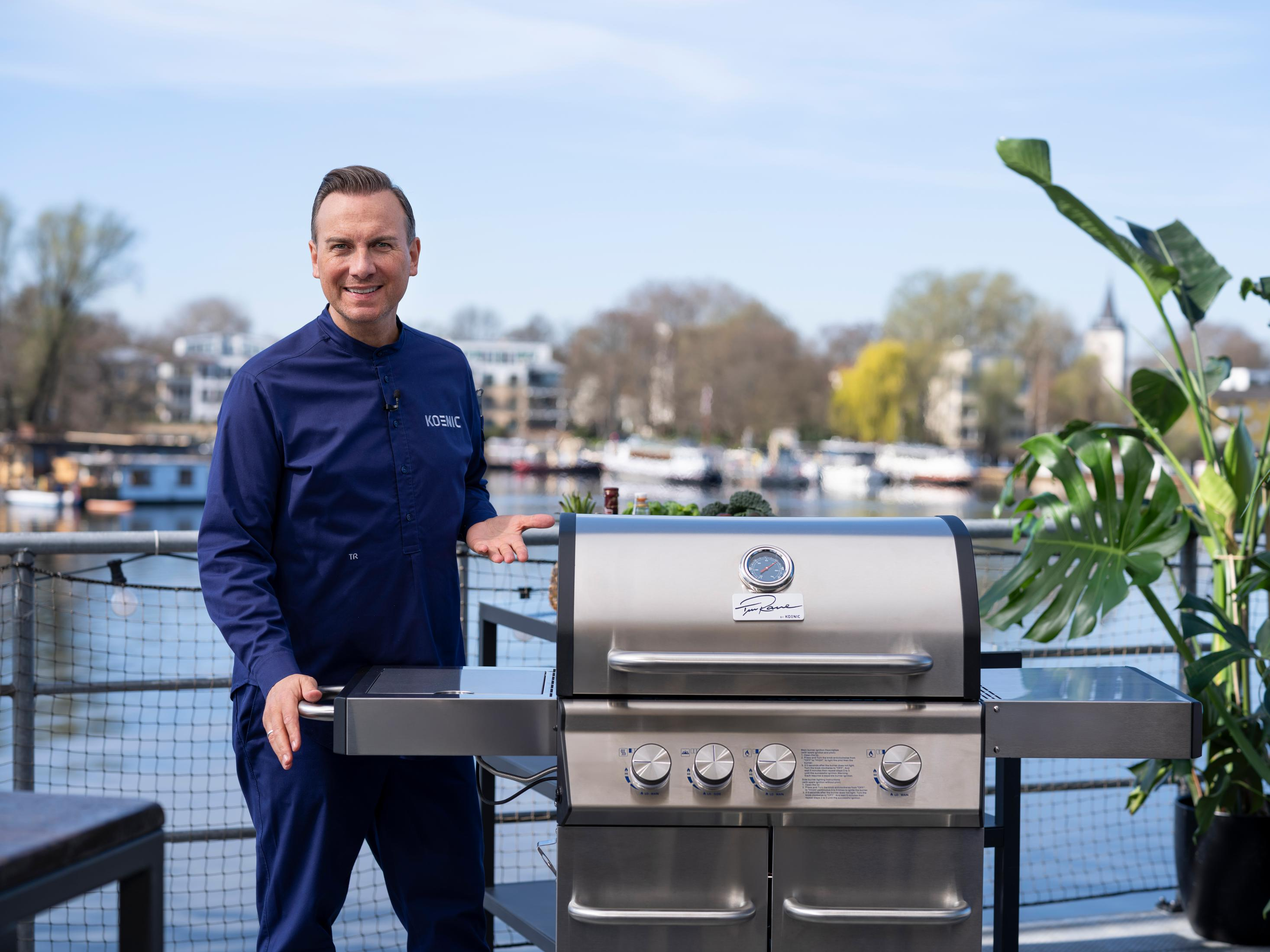 Mann steht neben einem Gasgrill aus Edelstahl auf einer Uferterrasse.
