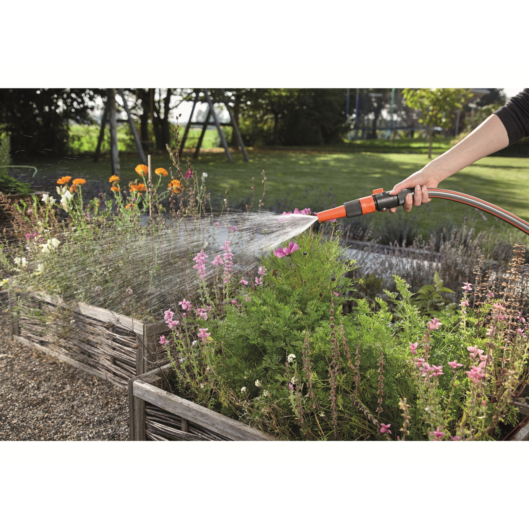 Eine Person bewässert Blumen mit einer orangefarbenen und schwarzen Gardena-Gartenschlauchdüse.