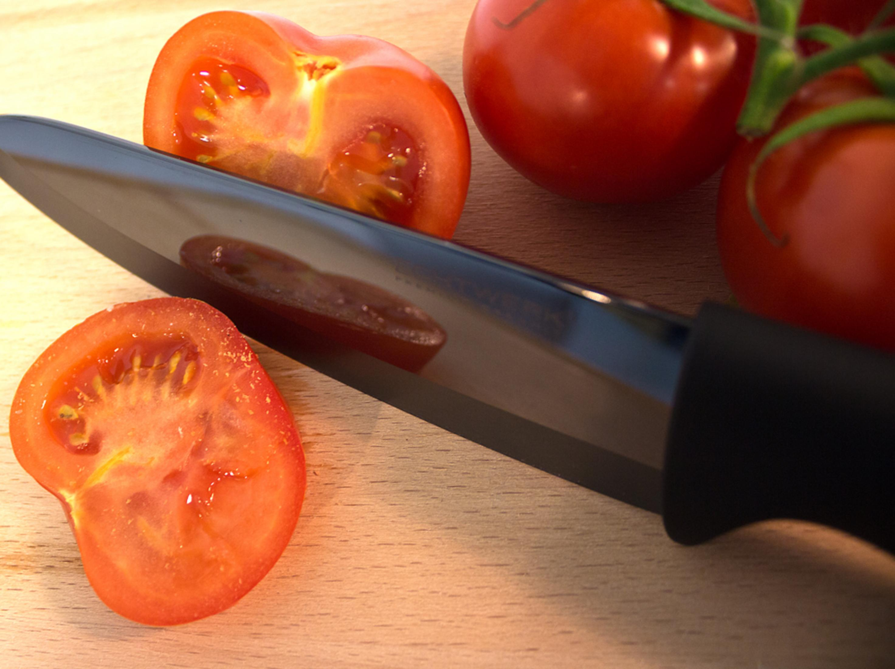 Ein schwarzes Keramikmesser schneidet Tomaten auf einem hölzernen Schneidebrett.