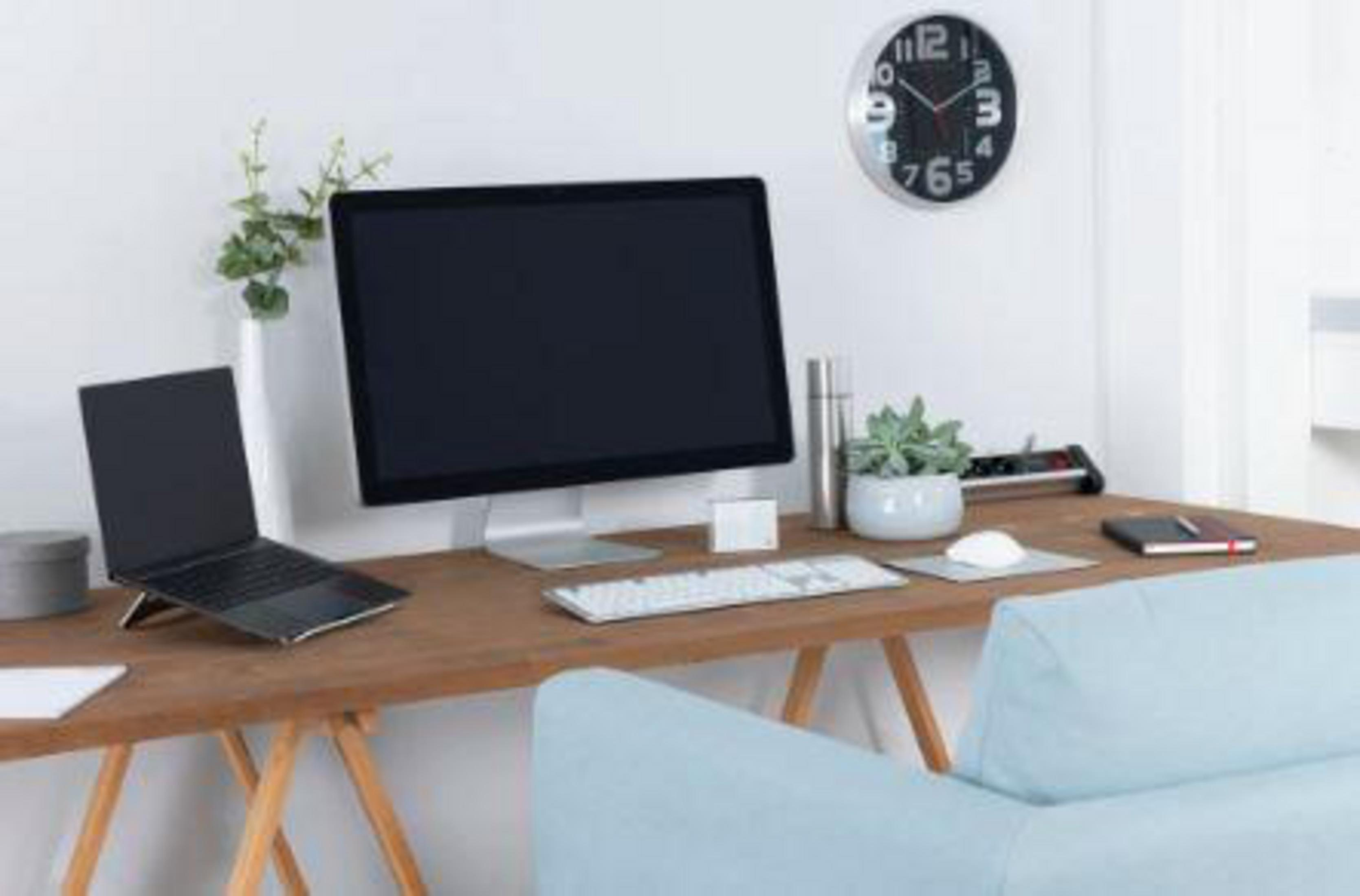 Ein moderner Arbeitsplatz mit einem Laptop auf einem Ständer, großem Monitor, Tastatur, Maus und einem hellblauen Sofa.