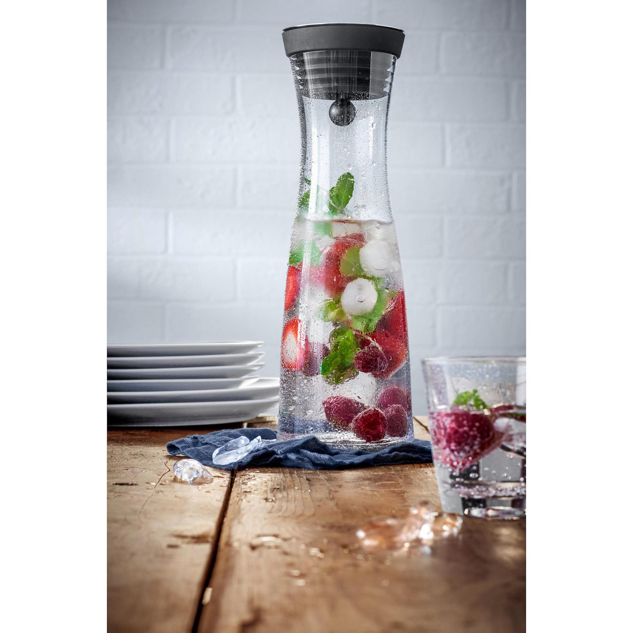 Wasserkaraffe mit Obst und Eis auf einem Holztisch.