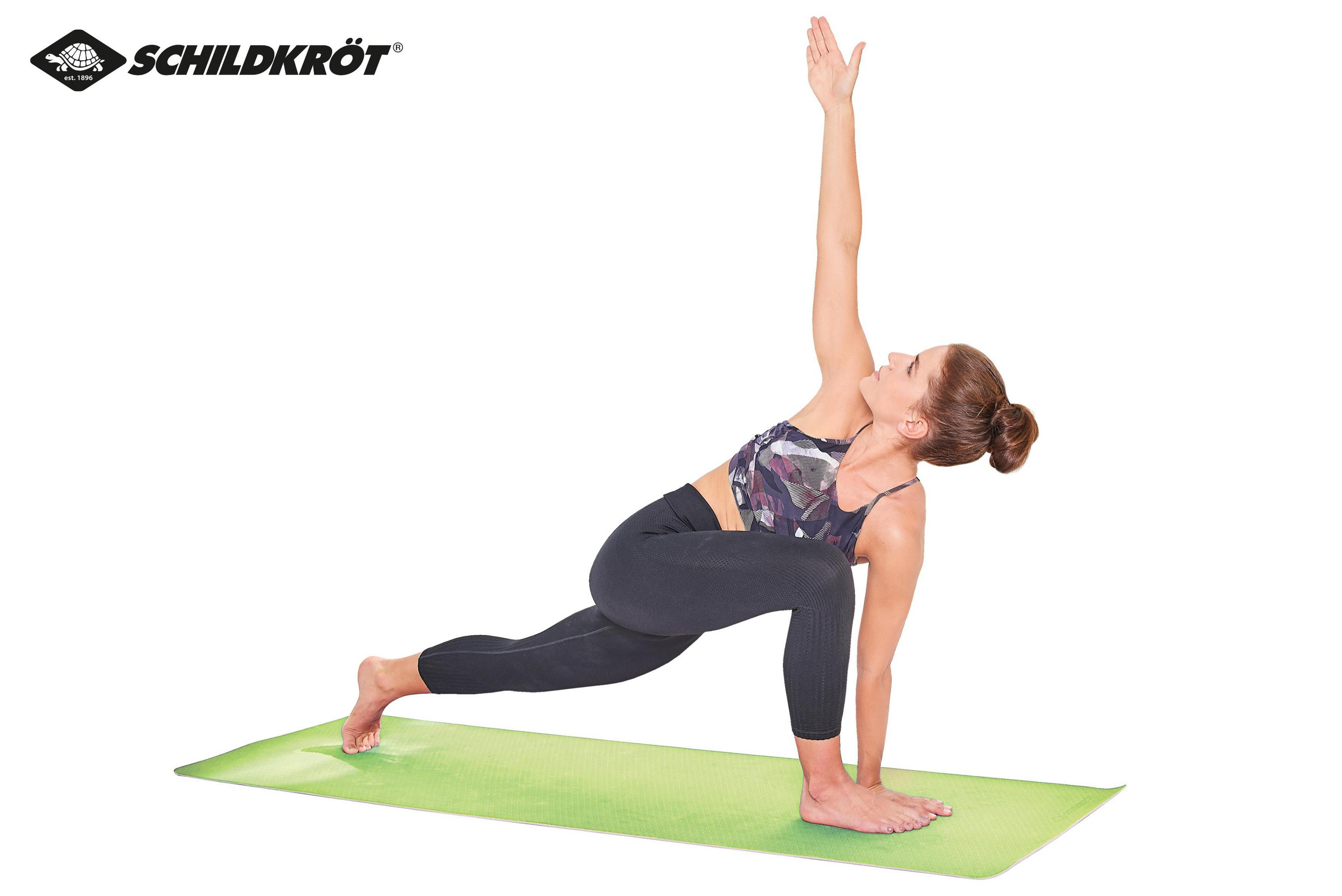 Eine Frau in Sportkleidung posiert in einer Yoga-Haltung auf einer grünen Matte vor einem weißen Hintergrund.