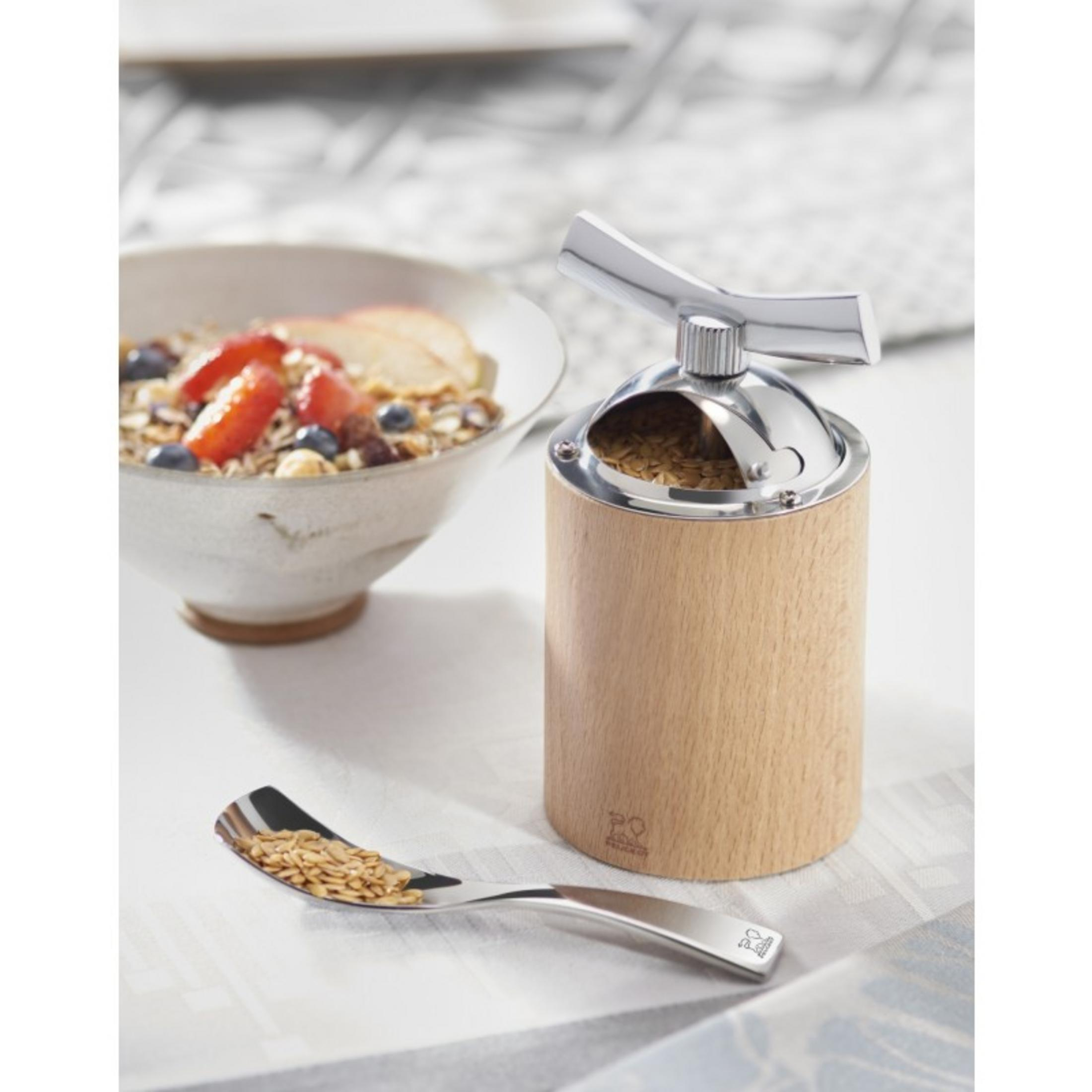 Eine Holzmühle steht in der Nähe einer Schüssel mit Müsli und einem Löffel Samen auf einem Tisch.
