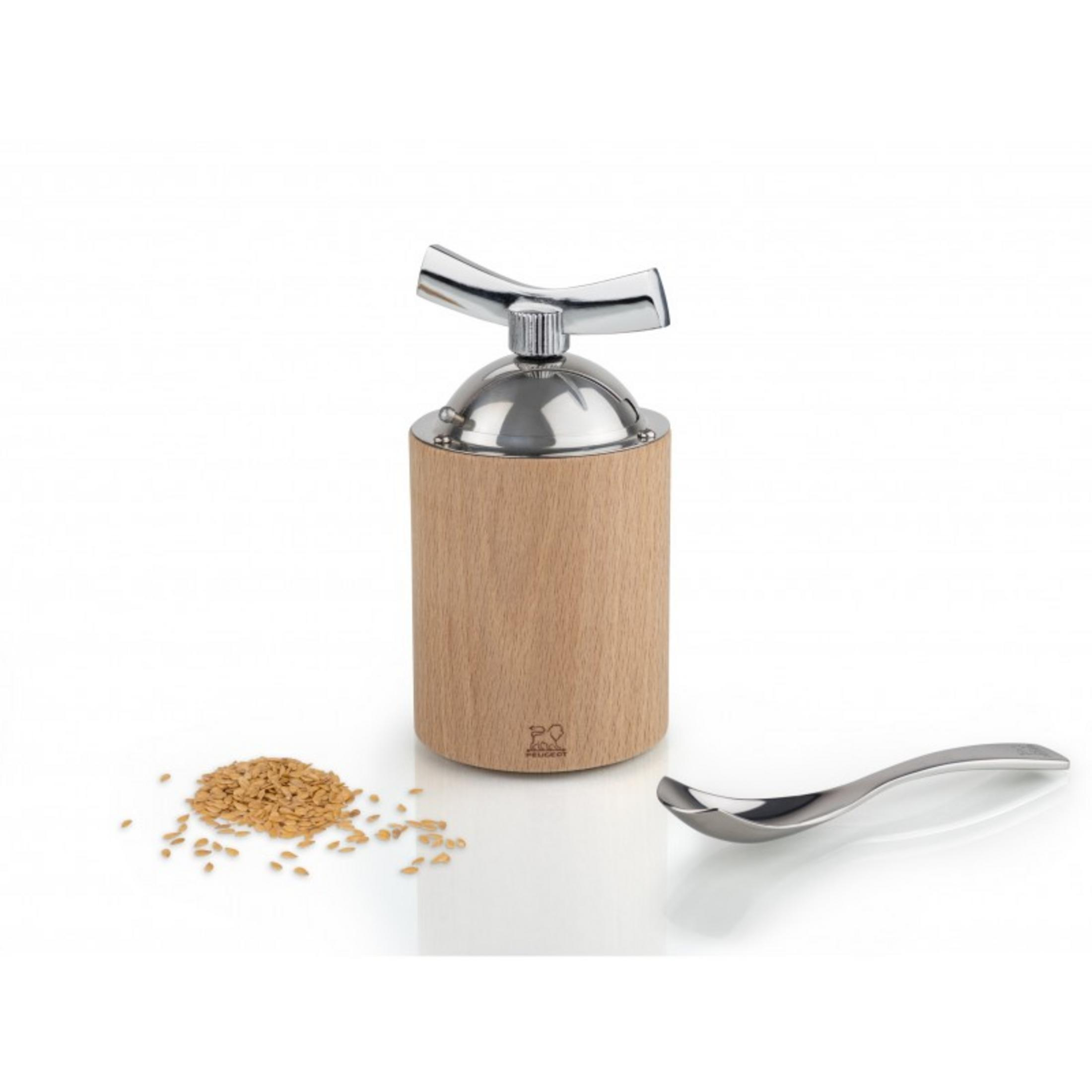 Eine Holzmühle steht in der Nähe eines Haufens Samen und eines Löffels auf einer weißen Oberfläche.