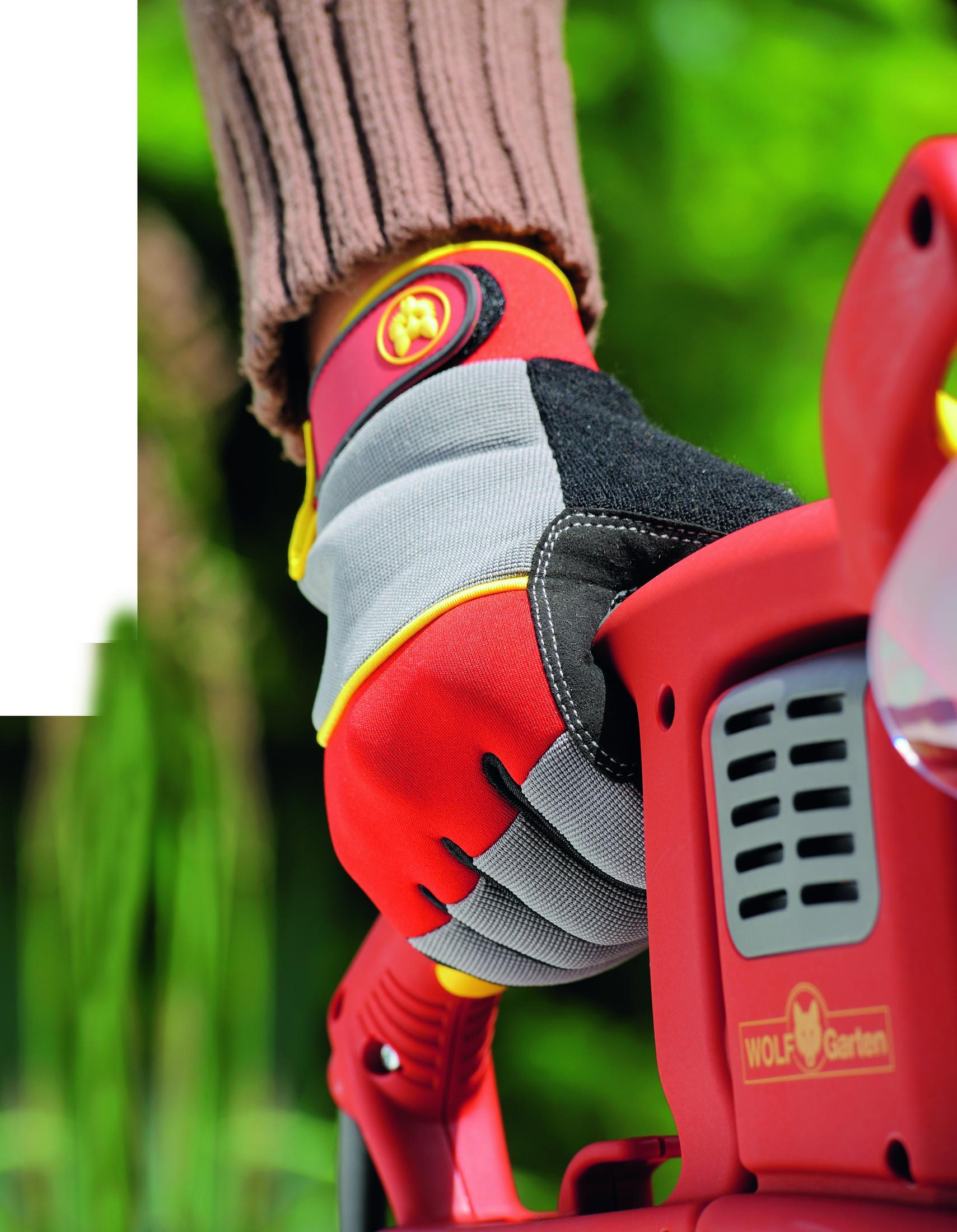 Eine Hand mit einem roten, grauen und schwarzen Arbeitshandschuh hält ein rotes Elektrowerkzeug.