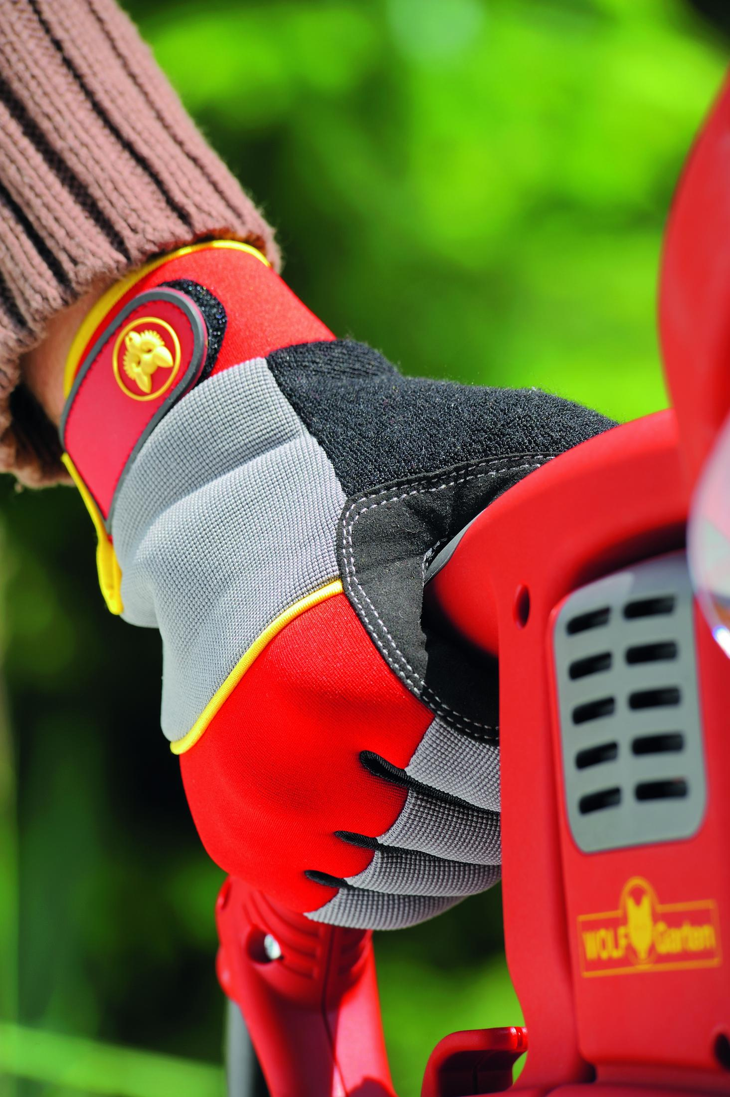 Ein roter, grauer und schwarzer Arbeitshandschuh hält ein rotes Elektrowerkzeug.