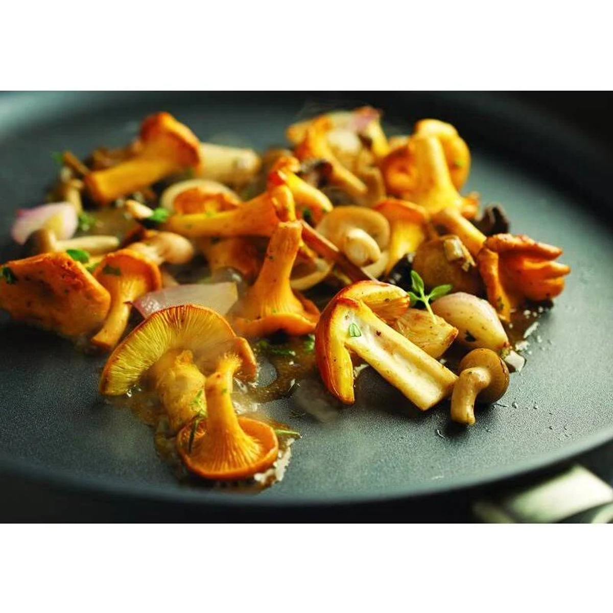 Une assiette noire avec des girolles sautées et des herbes. Les champignons sont dorés et entourés d'une sauce légère.
