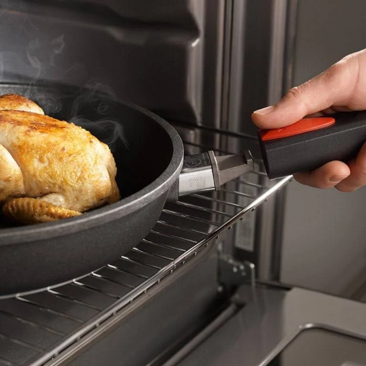 Une personne place une casserole avec un poulet cuit dans un four. La casserole a une poignée amovible.