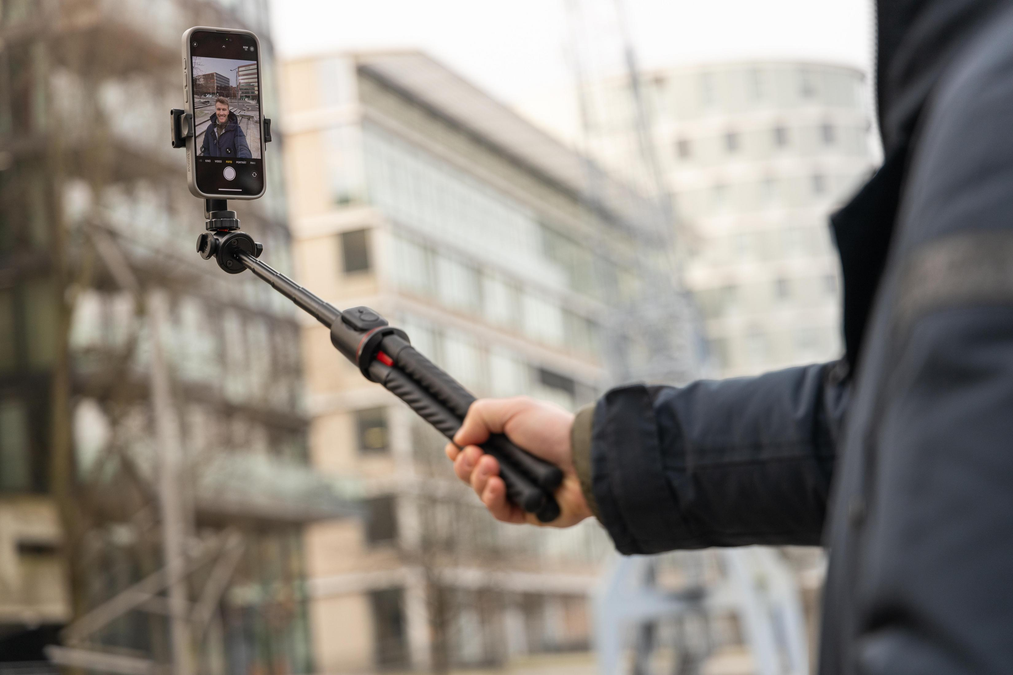 Persona che tiene in mano un bastone da selfie nero con un telefono attaccato.