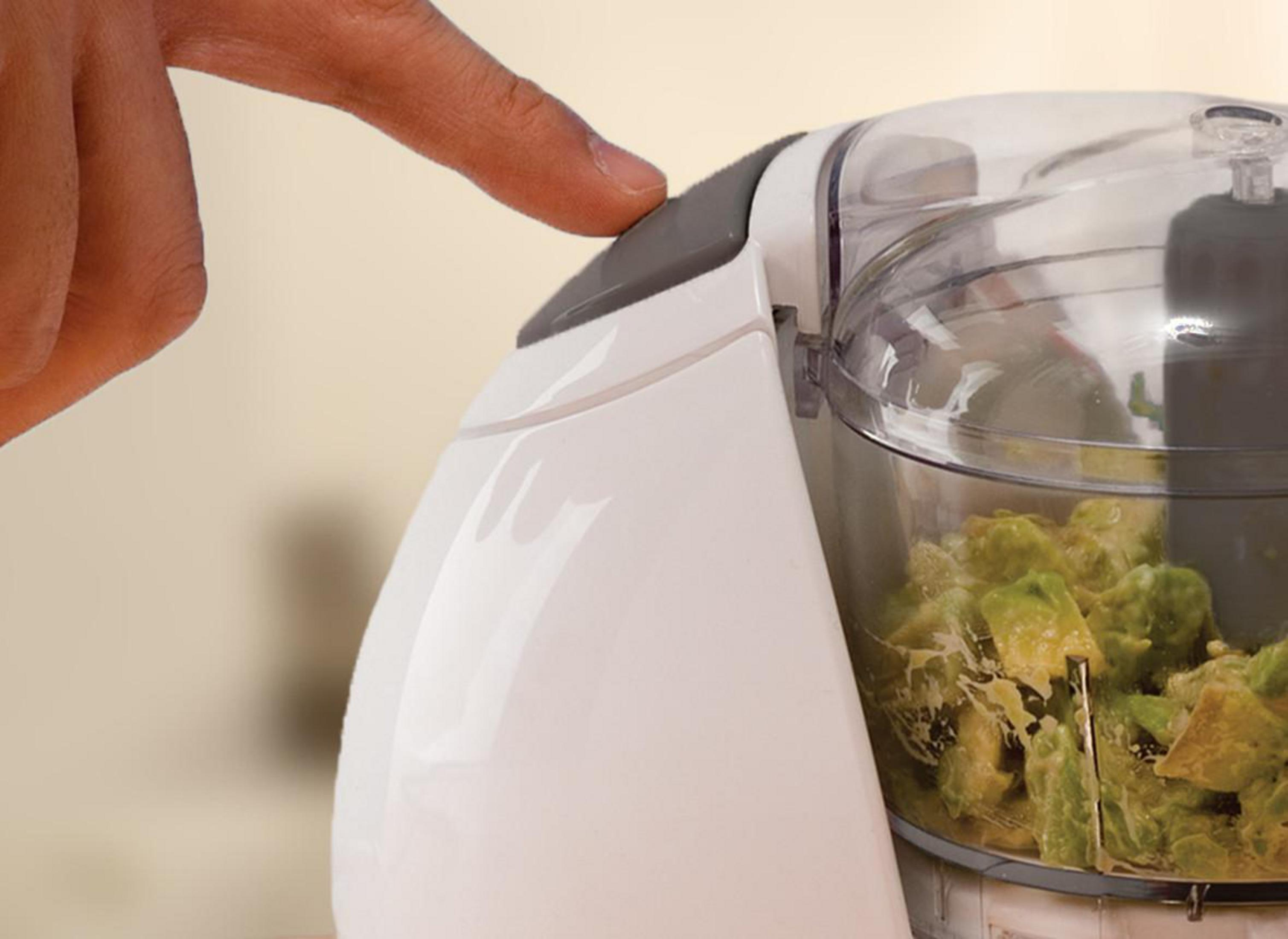 Ein Finger drückt den Netzschalter an einem Kenwood-Zerkleinerer, der mit Avocado gefüllt ist.