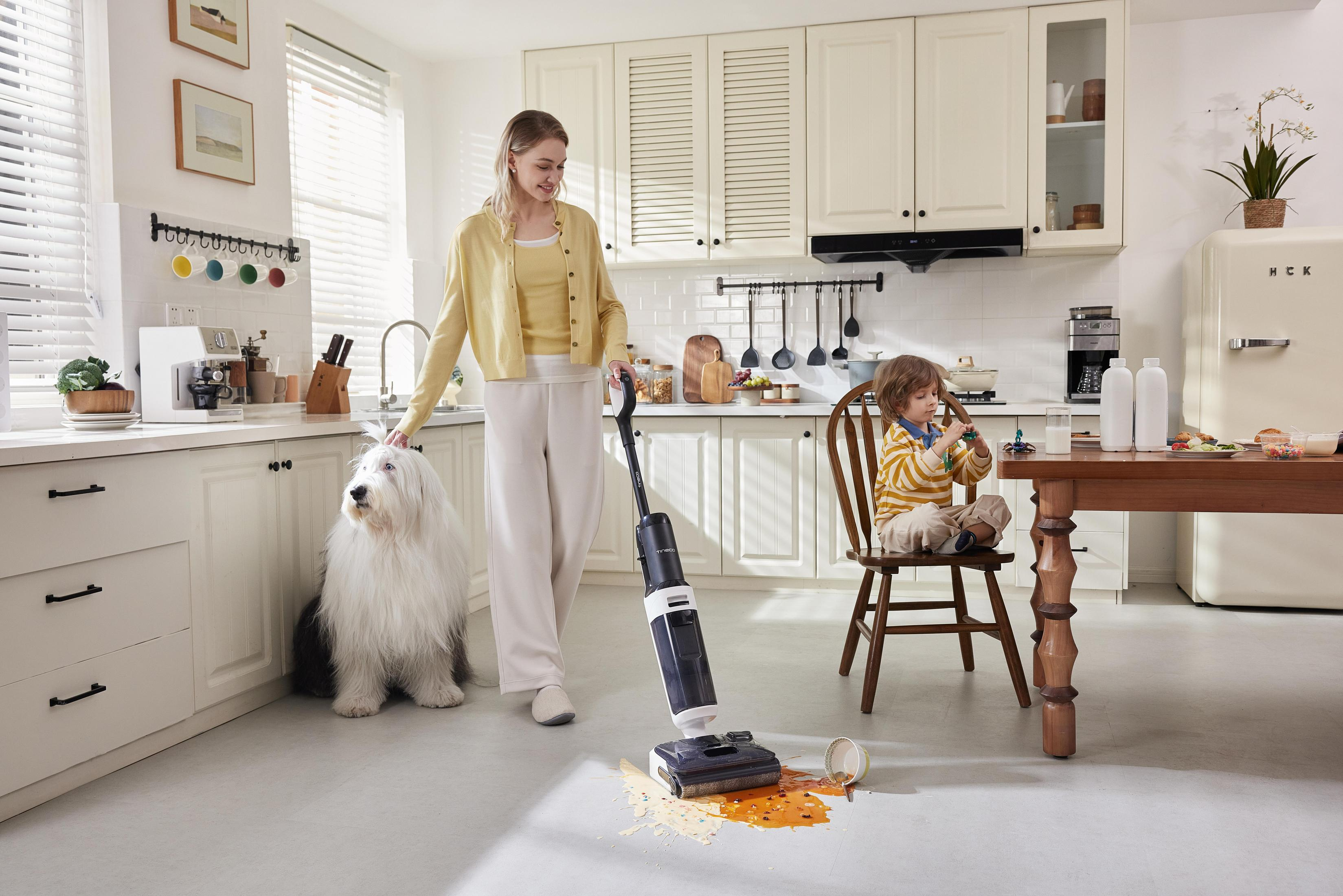 Kobieta odkurza w kuchni z dzieckiem i psem. Rozlana ciecz na podłodze. Atmosfera rodzinna.