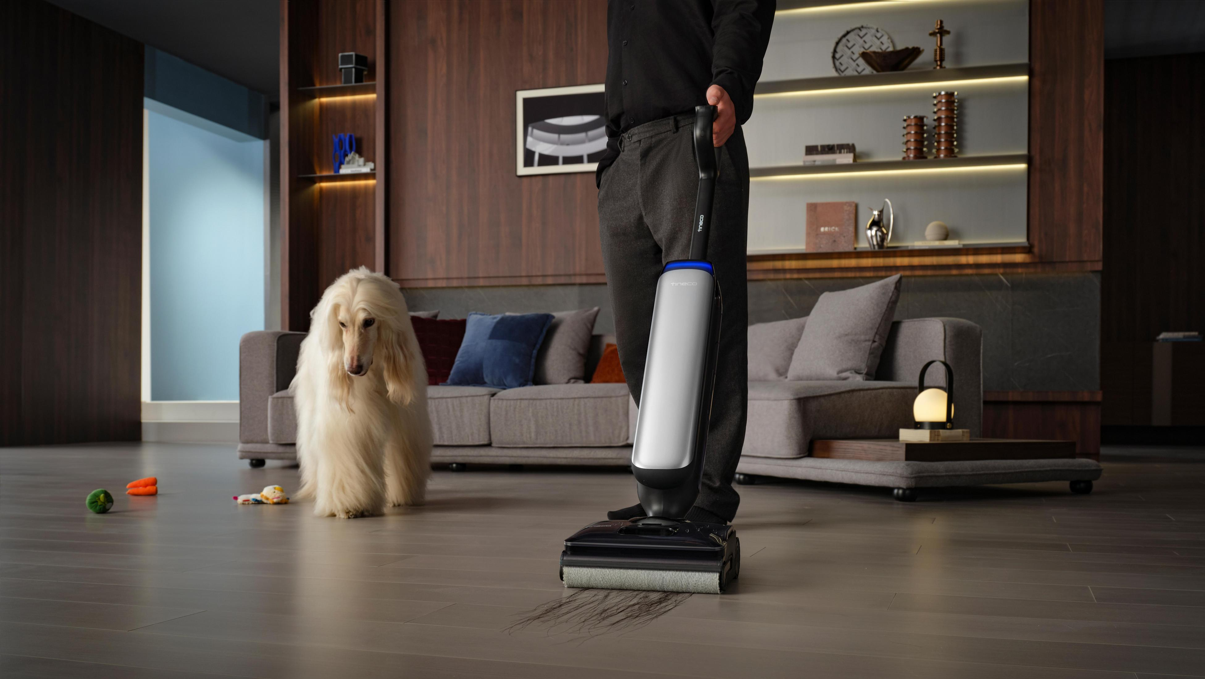 Mężczyzna używający środka do czyszczenia podłóg. Pies siedzi na podłodze. Salon z drewnianą podłogą.