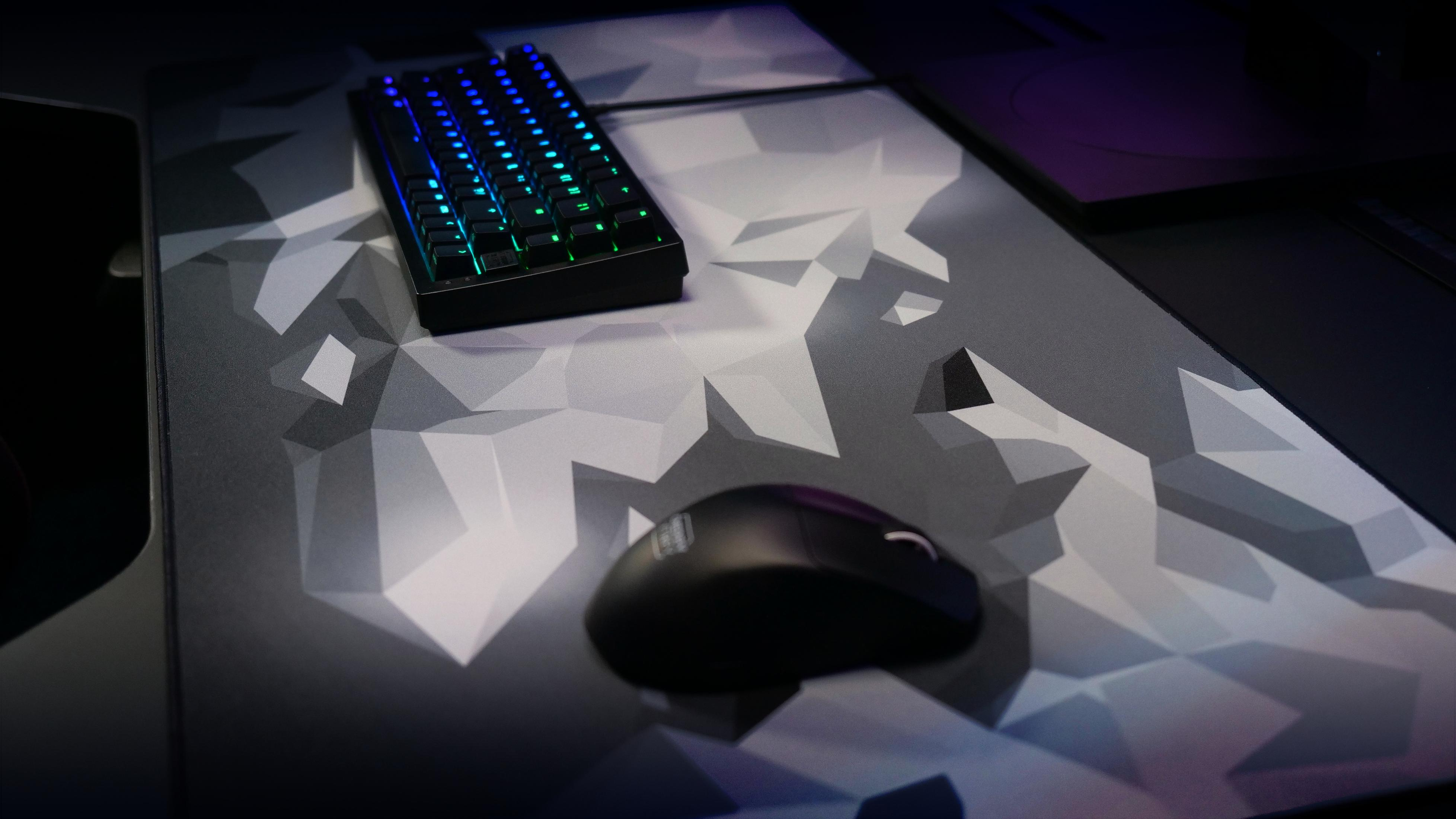 Ein Gaming-Setup mit Tastatur, Maus und Mauspadd. Die Tastatur hat bunte Beleuchtung. Das Mauspadd hat ein geometrisches Design.