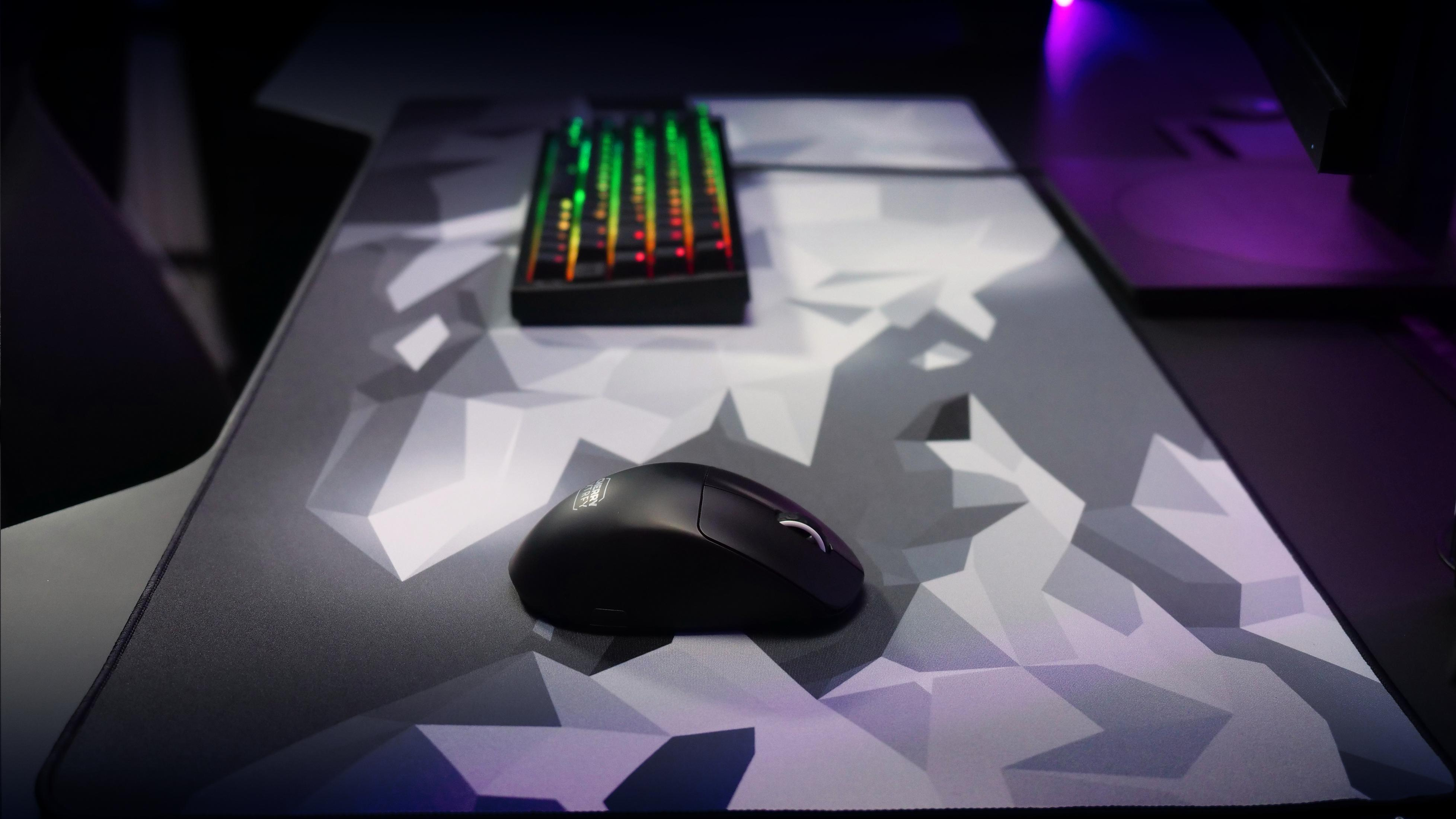 Eine schwarze Maus liegt auf einem geometrisch gemusterten Mauspads. Im Hintergrund befindet sich eine Tastatur.