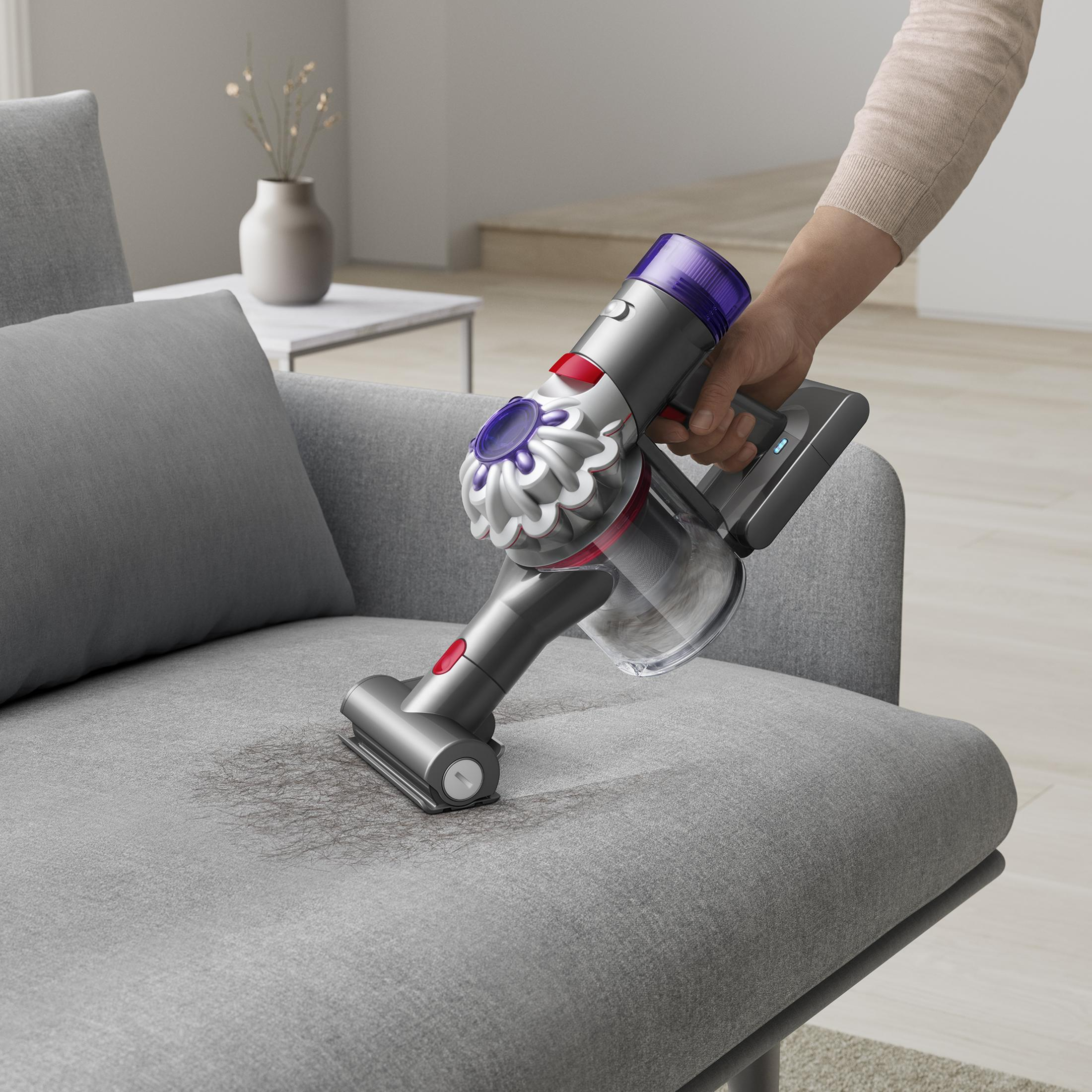 Eine Person saugt ein graues Sofa mit einem Dyson Akku-Staubsauger.