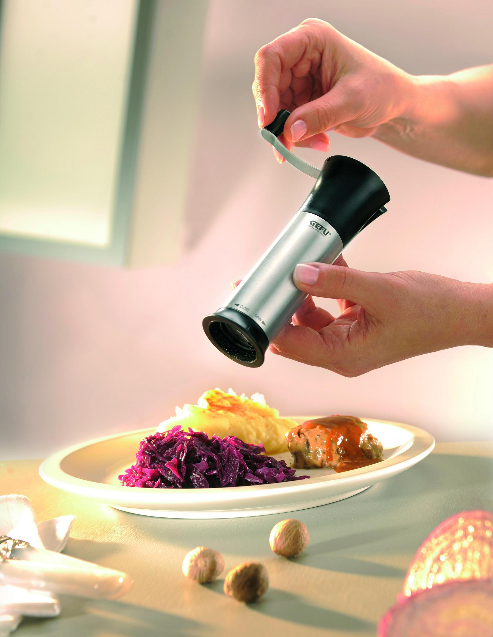 Eine Person mahlt mit einer GEFU-Gewürzmühle Gewürze über einem Teller mit Essen.