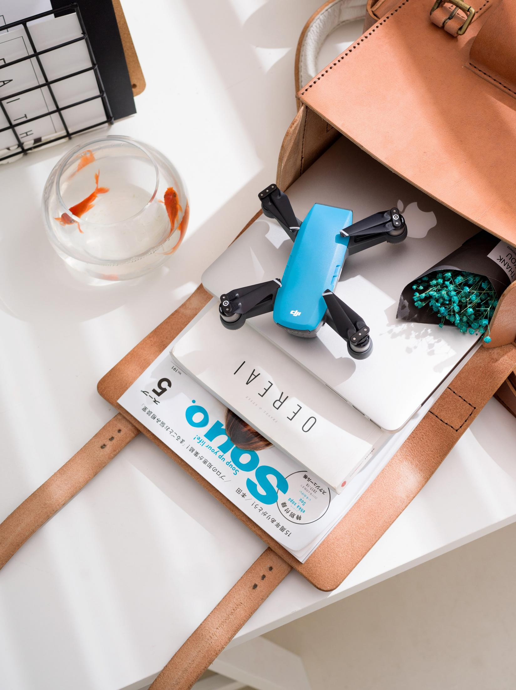 Drohne, Laptop, Zeitschriften und ein Fischglas in einer offenen Tasche.