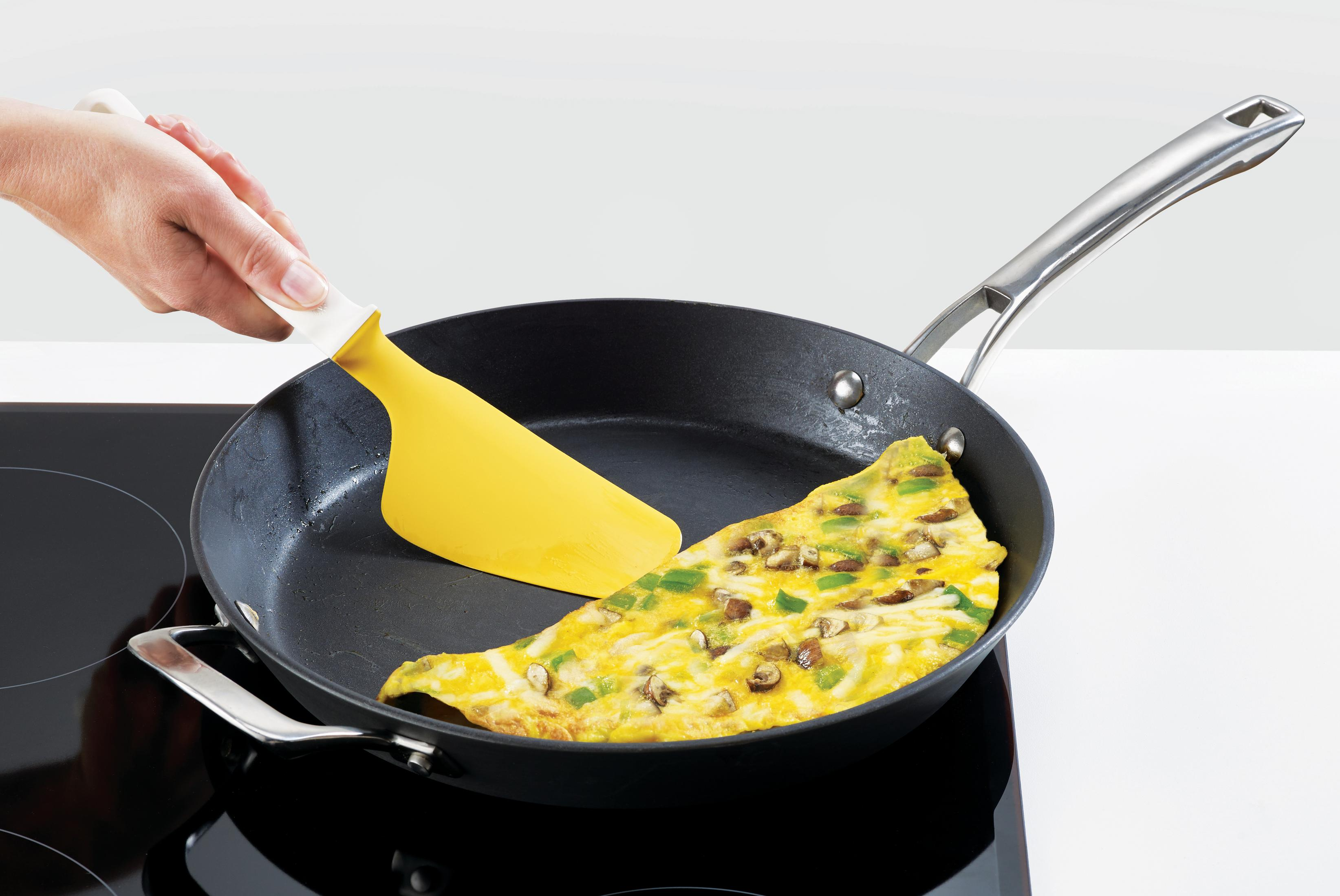 Sarı spatula, ocağın üzerinde siyah bir tavada omleti çeviriyor. Omletin içinde yeşil biber ve mantar var.