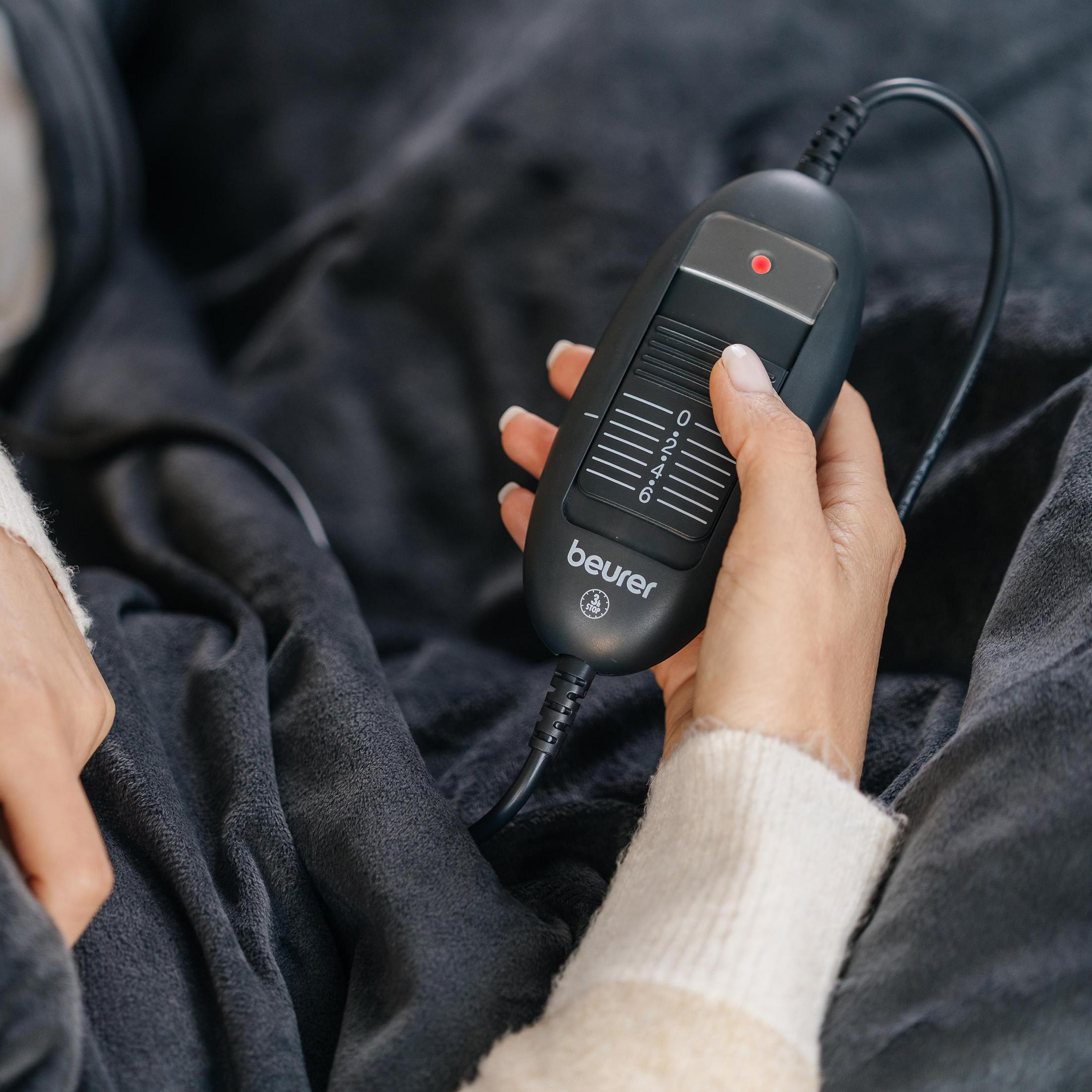Eine Hand justiert den schwarzen Controller einer grauen Heizdecke mit den Einstellungen 0 bis 6.