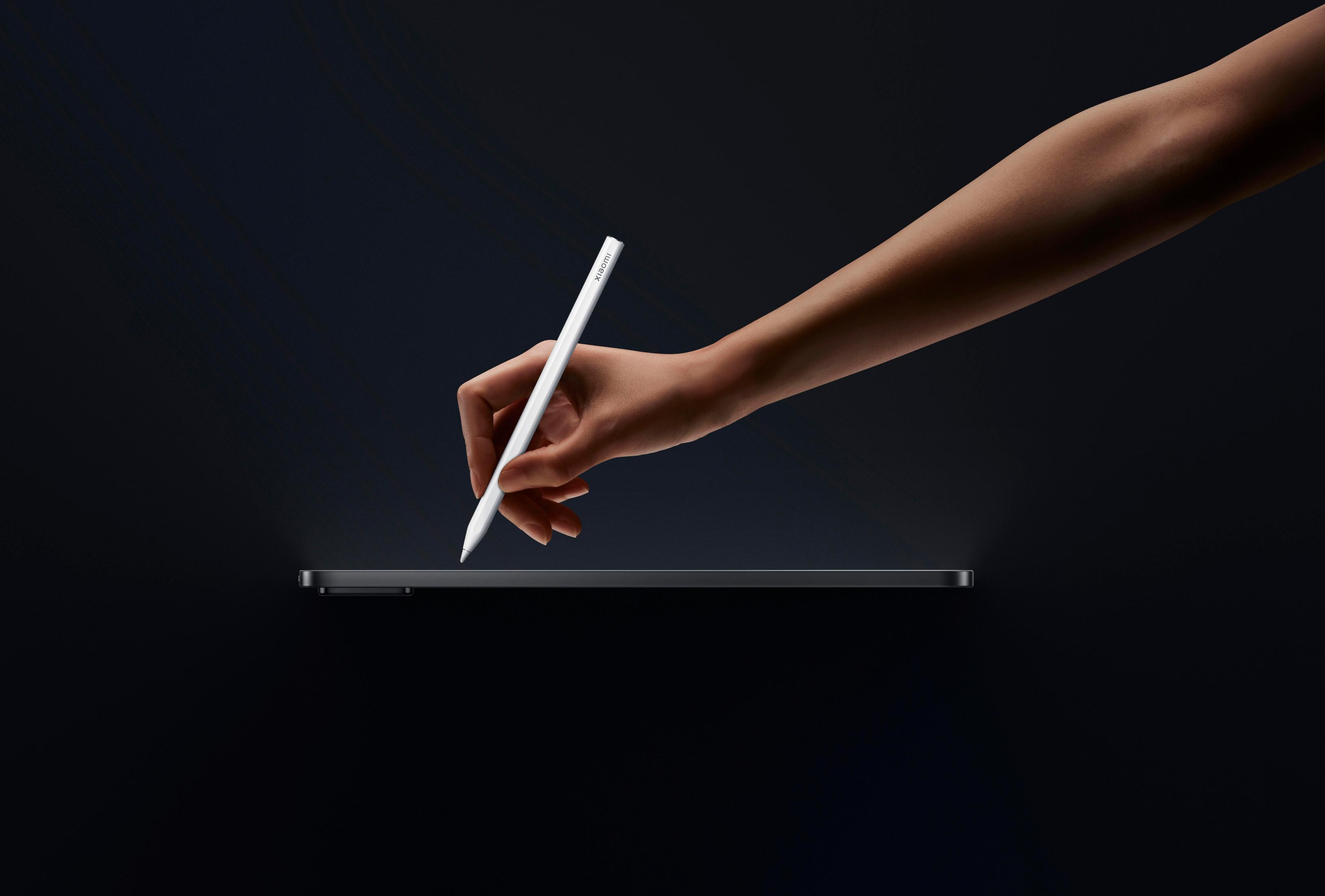 Eine Hand hält einen weißen Stift über einem dunklen Tablet vor einem dunklen Hintergrund.