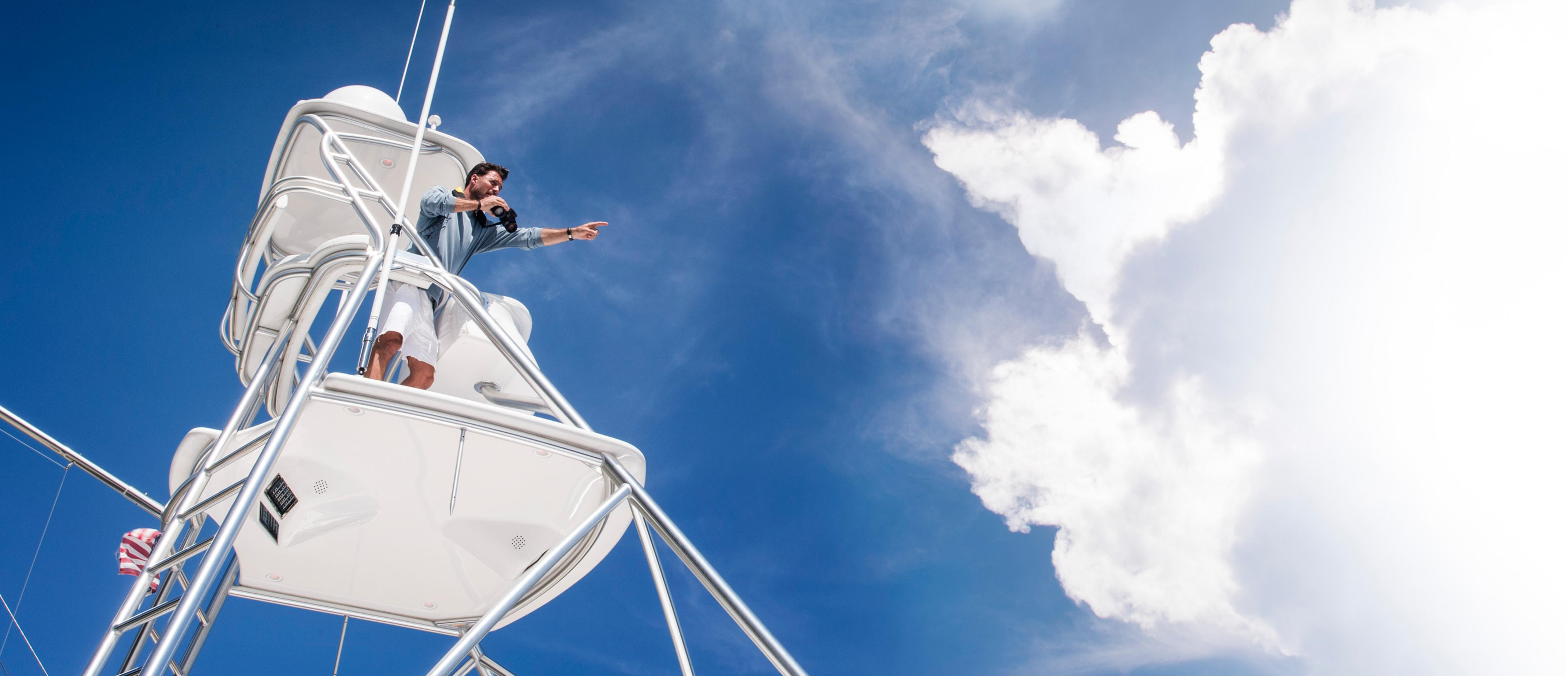 Ein Mann mit Fernglas steht auf einem weißen Turm vor einem blauen Himmel mit weißen Wolken.