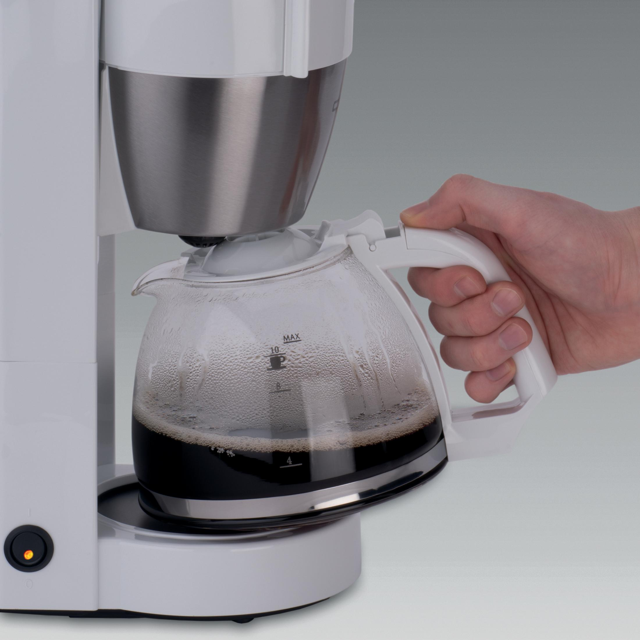 Eine Hand entfernt eine Glaskaraffe mit dunklem Kaffee aus einer weißen Kaffeemaschine.