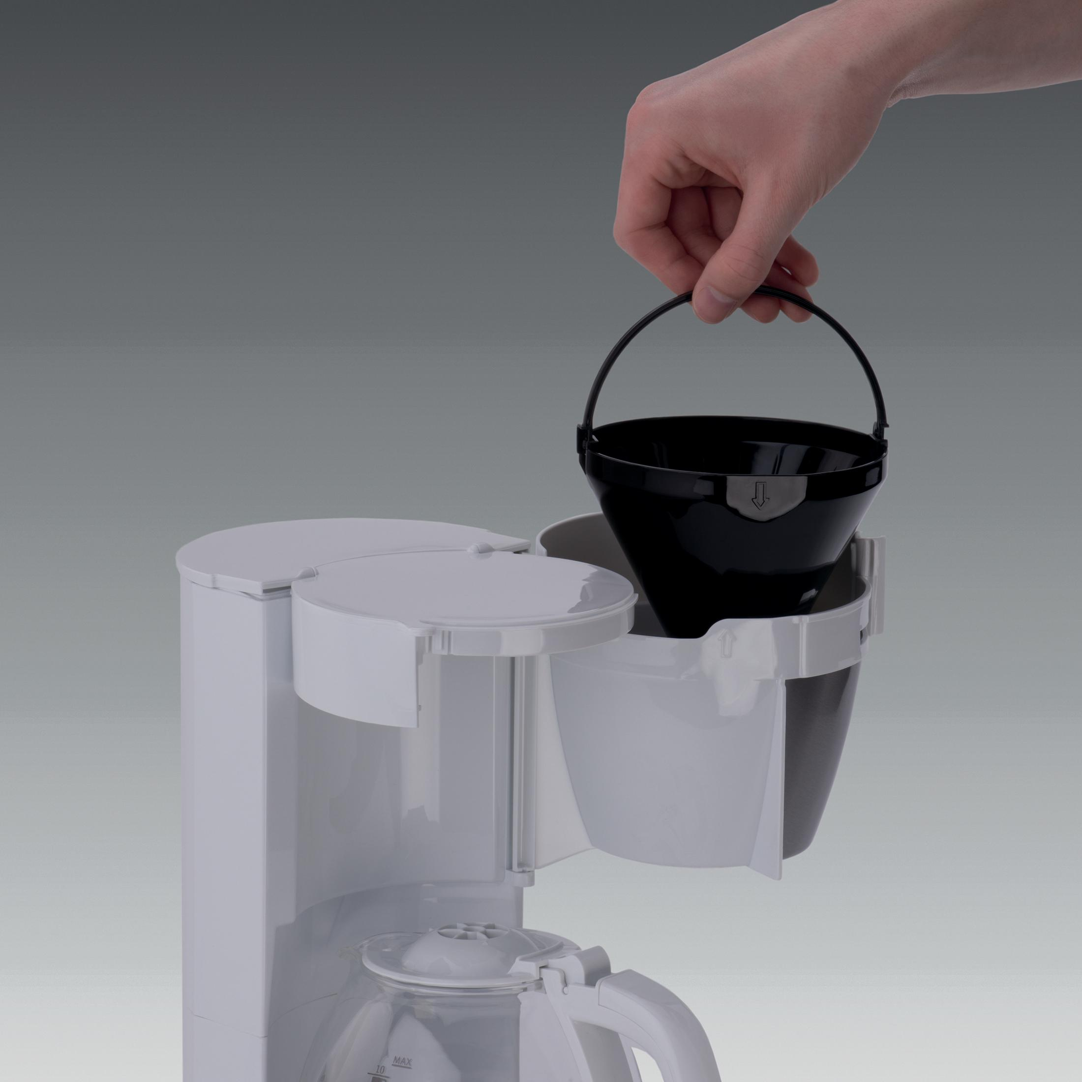 Eine Hand wird gezeigt, die einen schwarzen Filter in eine weiße Kaffeemaschine legt. Grauer Hintergrund.