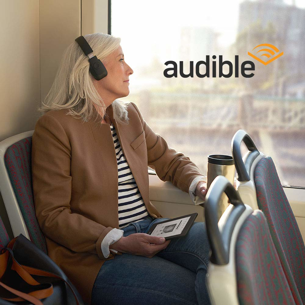 Frau im Zug, hört Audio mit Kopfhörern, liest ein Buch. Audible-Logo.