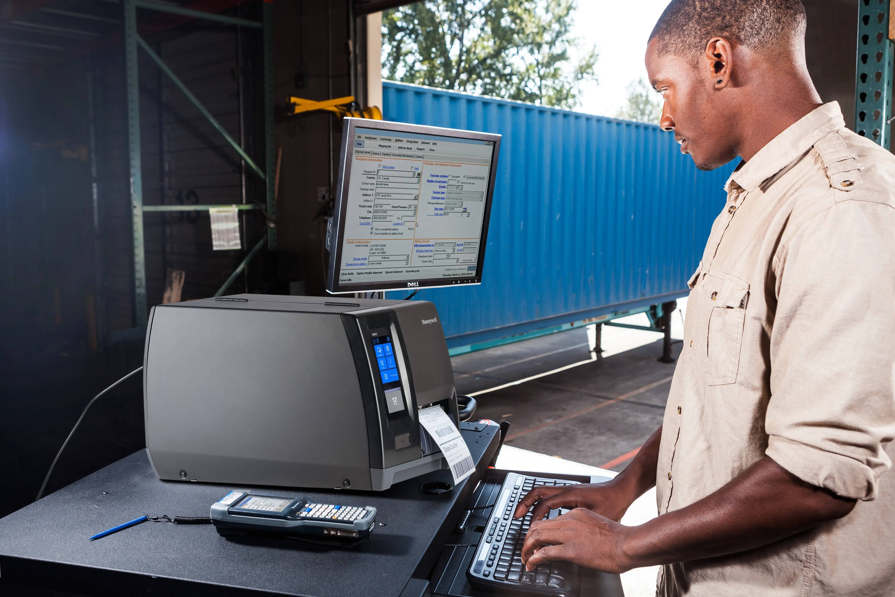Mężczyzna pisze na klawiaturze, przed nim drukarka etykiet i monitor komputera.