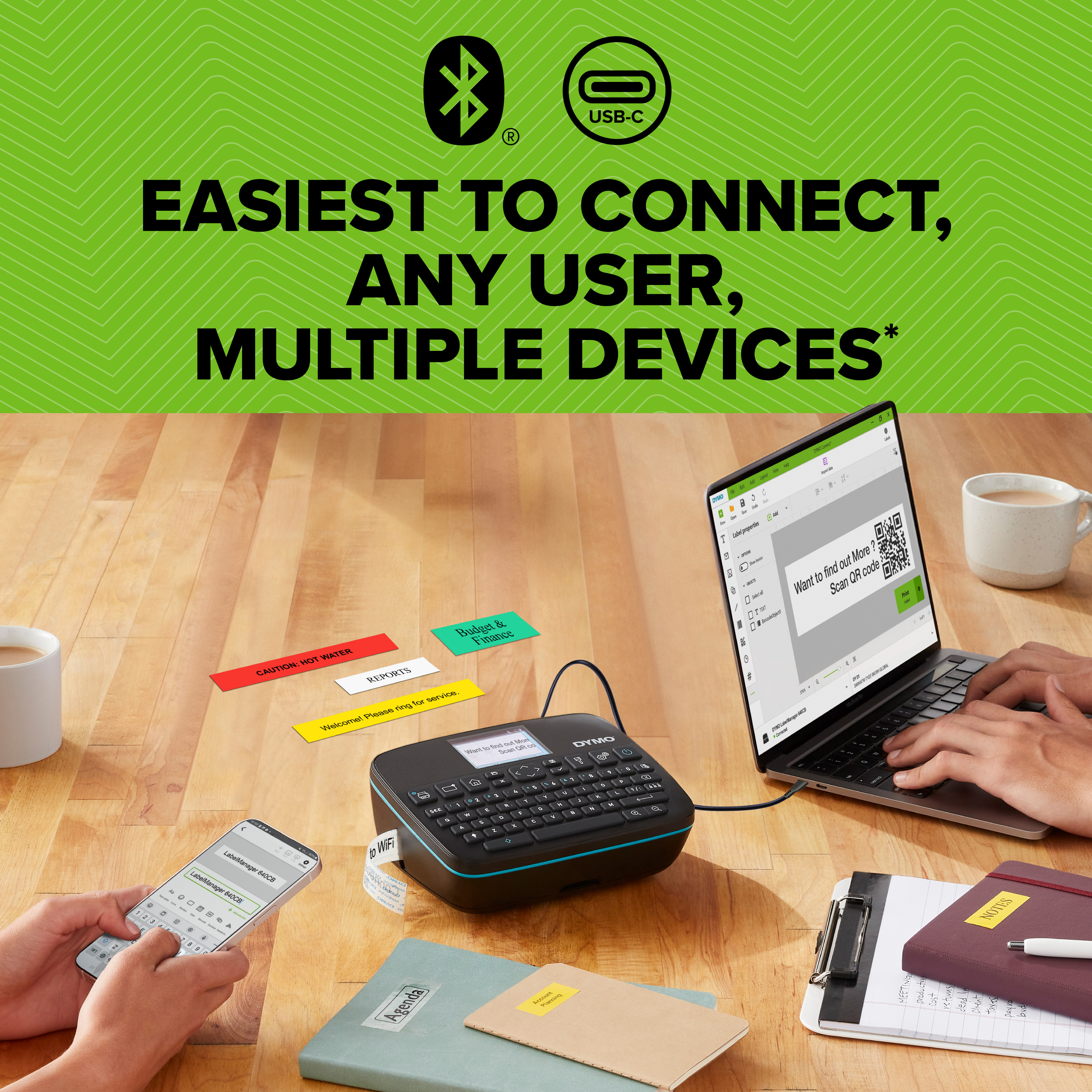 Ręce używają etykieciarki DYMO podłączonej do laptopa, z różnymi oznaczonymi przedmiotami na drewnianym stole.