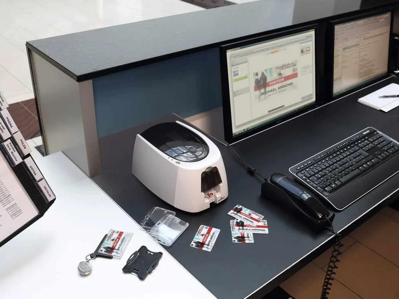 Una stampante per carte Durable bianca su una scrivania nera, con computer e carte d'identità nelle vicinanze.