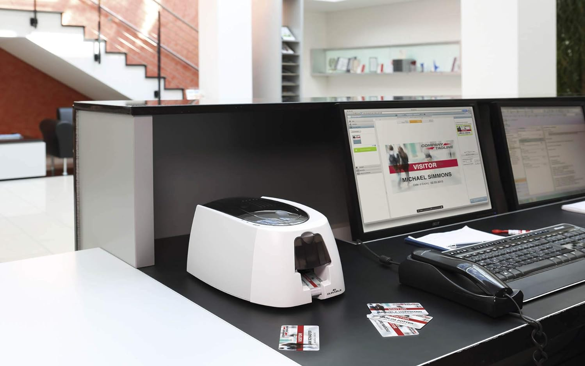 Una stampante per carte bianca è su una scrivania nera con computer, un telefono e carte.