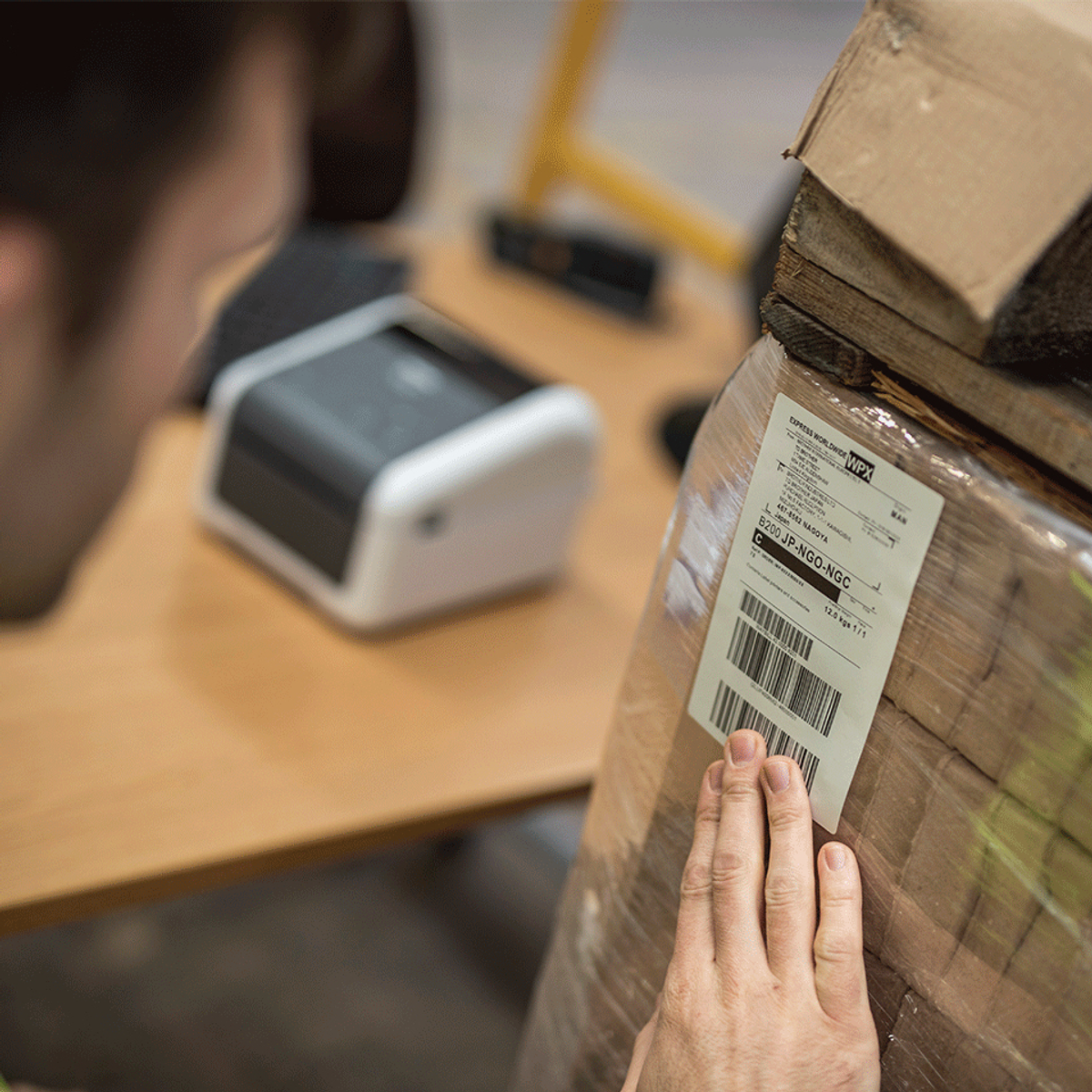 Ein Mann betrachtet ein Paket mit einem Etikett. Ein Etikettendrucker steht auf dem Tisch.